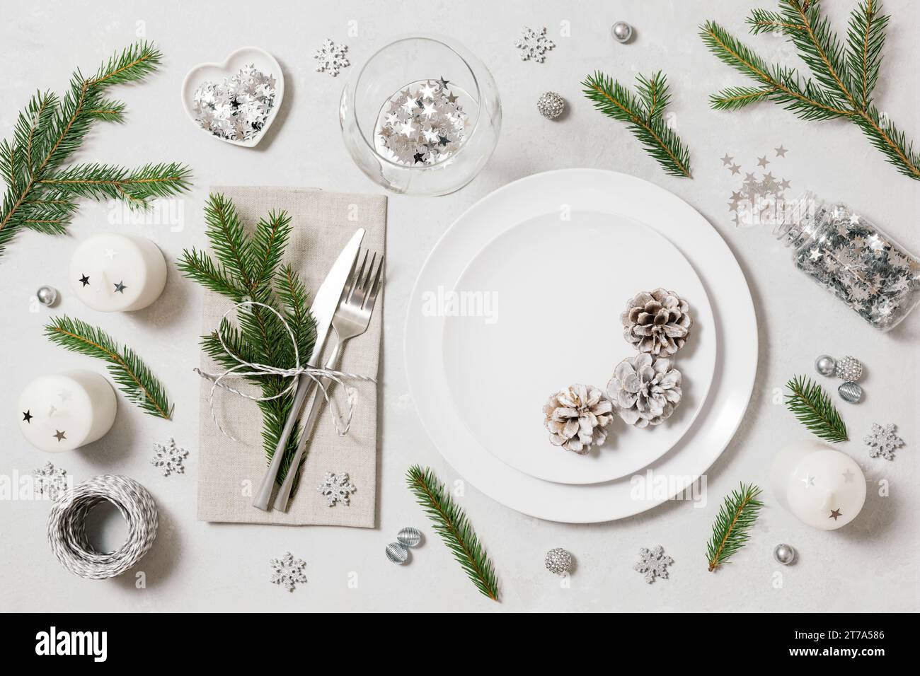 Tavolo festivo per la cena di Natale su sfondo bianco. Capodanno con decorazioni in argento, rami di abete e coni. Vista dall'alto. Foto Stock