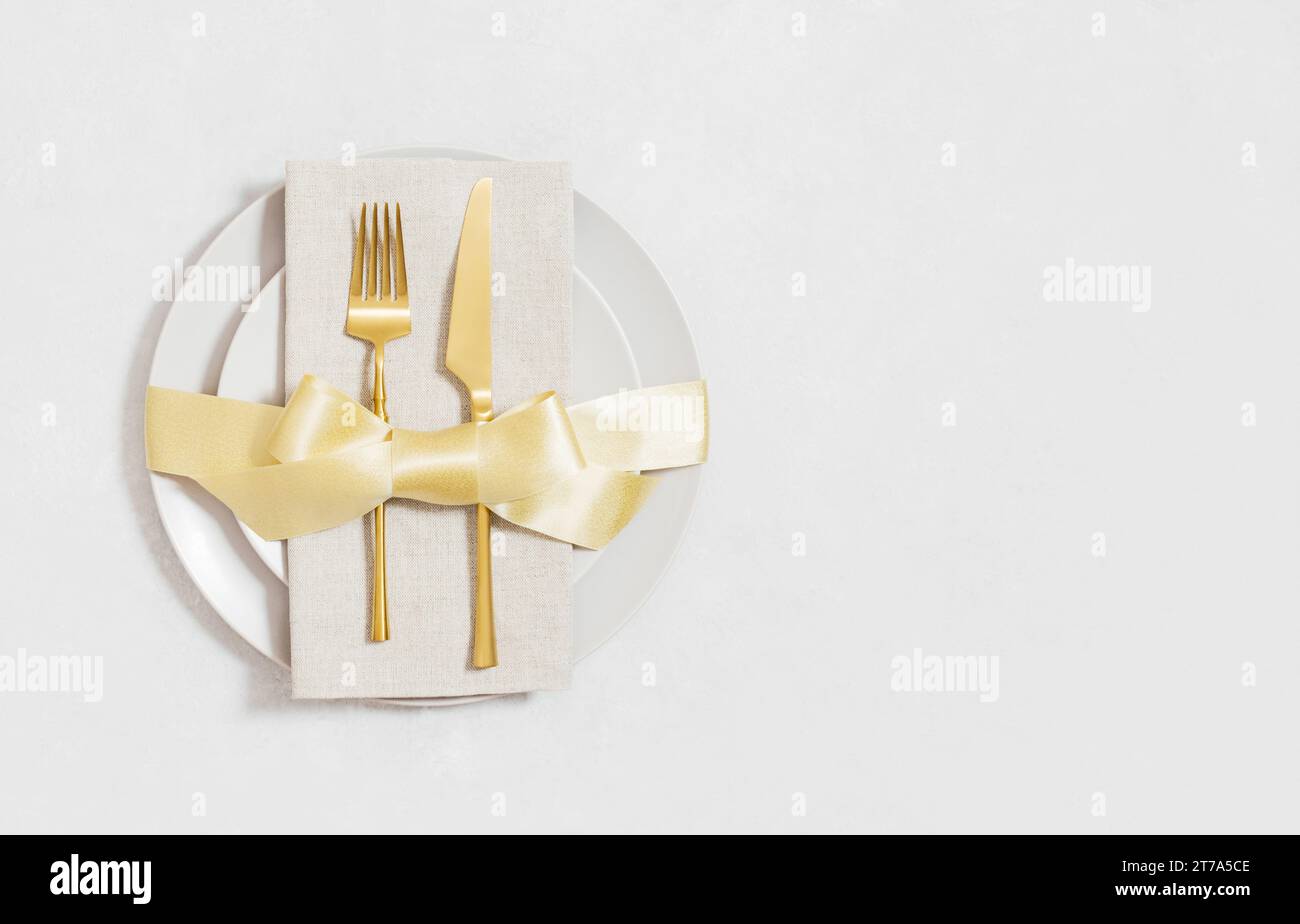 Ambiente da tavolo festivo con posate dorate in un piatto con fiocco. Servizio natalizio su sfondo bianco con spazio per la copia. Vista dall'alto, base piatta. Foto Stock