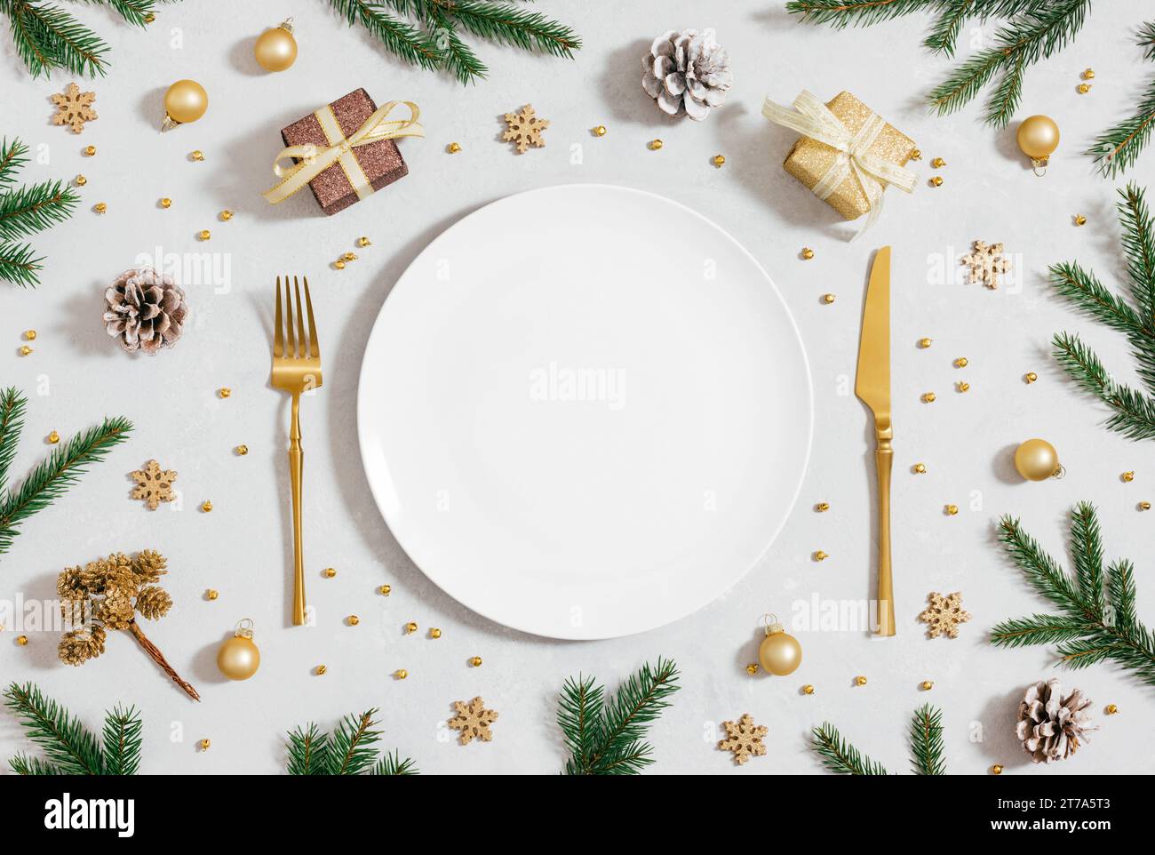 Tavolo dorato per la cena di Natale. Servizio di Capodanno con piatto bianco vuoto, rami di abete e accessori dorati. Vista dall'alto, base piatta. Foto Stock