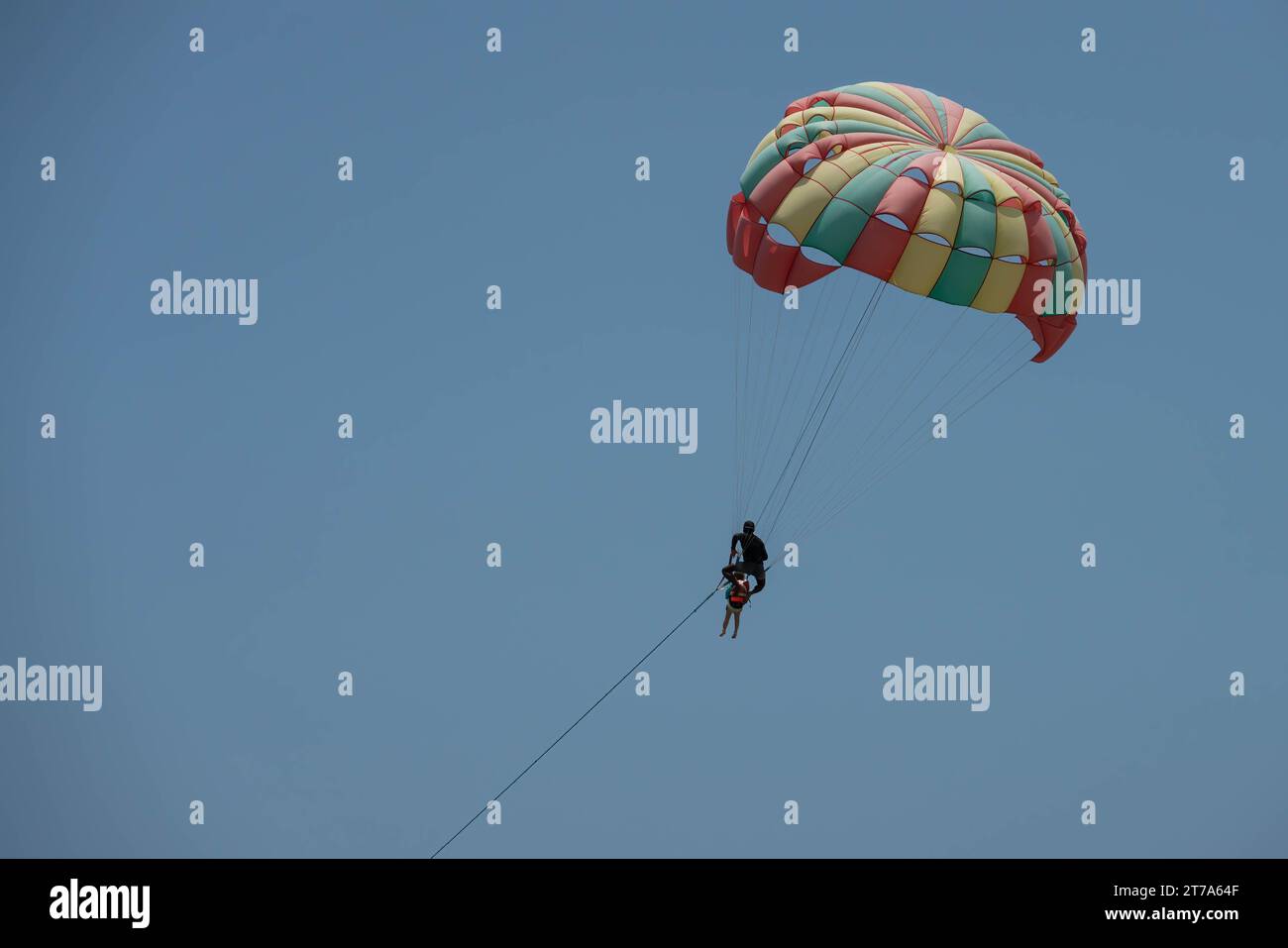 Due persone - uomo e bambino stanno paracadutizzando. Paracadute colorato, l'uomo tiene da dietro un bambino. Primo piano della foto su un cielo blu cristallino Foto Stock