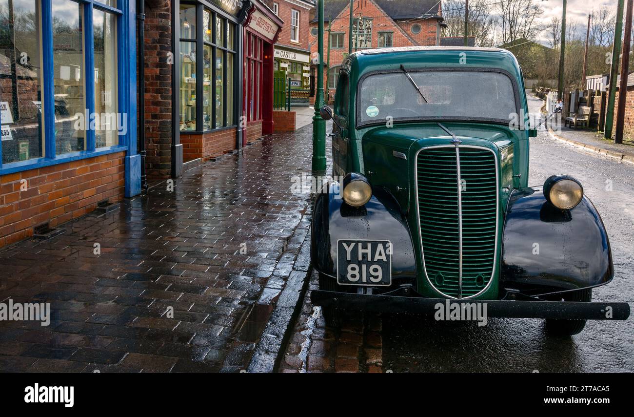 Un camion verde d'epoca si trova su una strada bagnata di ciottoli, circondata da affascinanti negozi di mattoni. Black Country Museum, Dudley, Inghilterra, Regno Unito Foto Stock