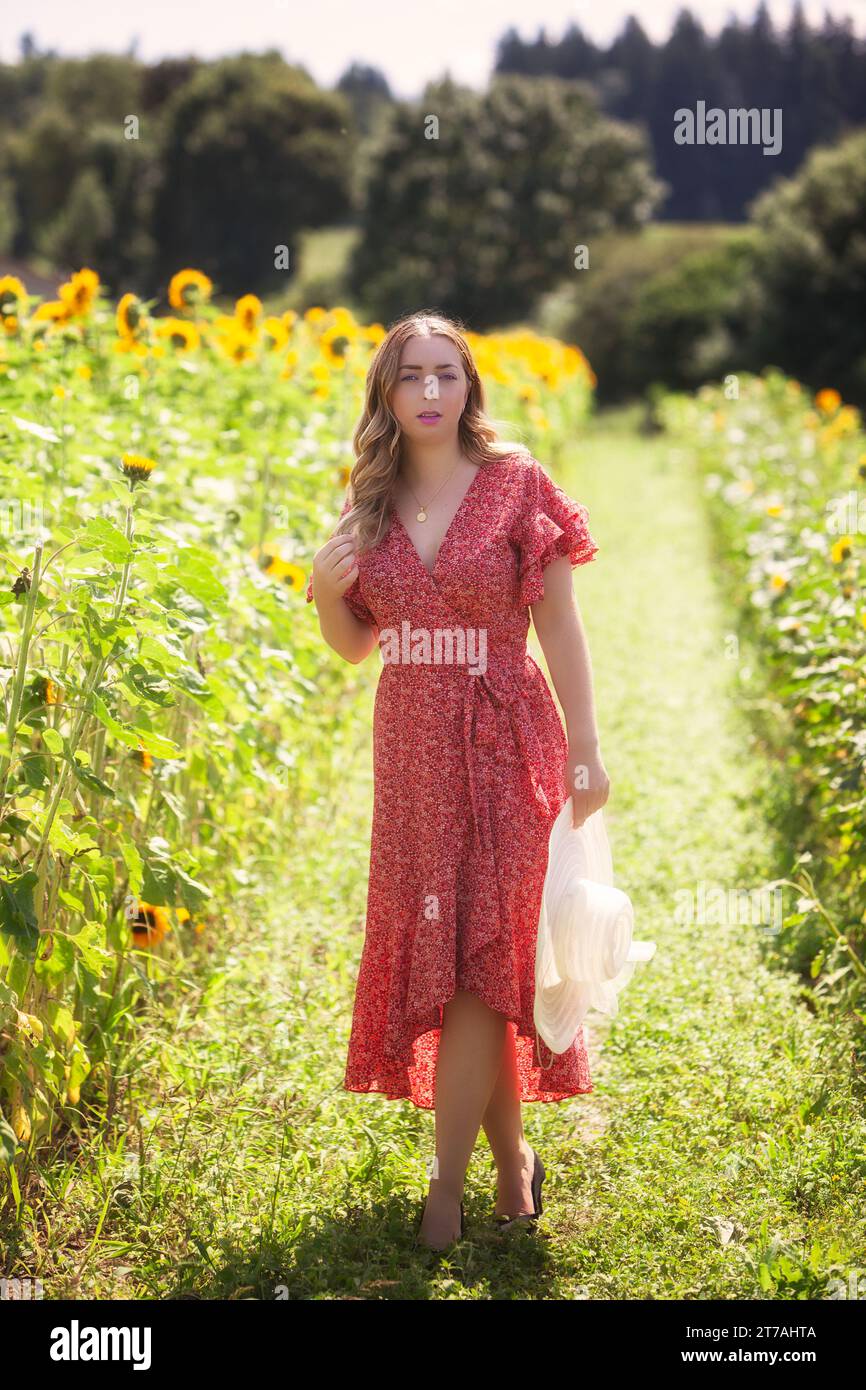 Giovane donna alla moda con cappello in mano, in piedi in un campo di girasoli Foto Stock
