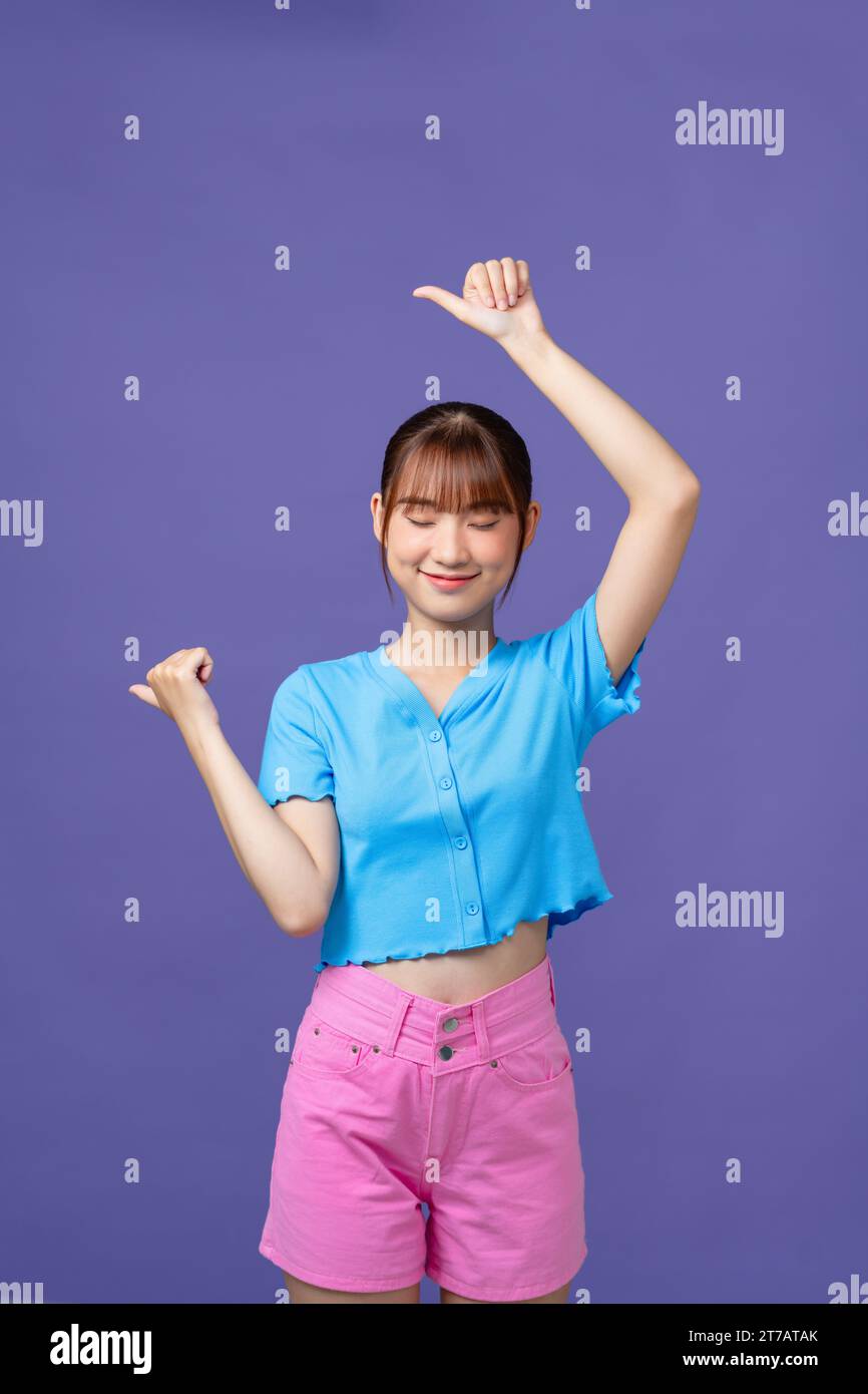 Giovane ragazza asiatica in piedi, puntando dietro la schiena con la mano e i pollici in alto, sorridendo fiduciosa Foto Stock