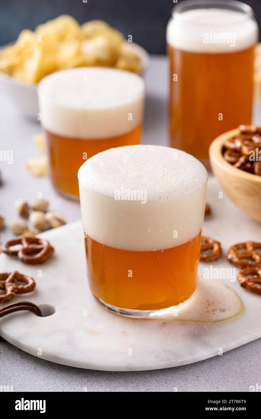 Birra lager in bicchieri con una varietà di spuntini, pretzel, patatine fritte e pistacchi Foto Stock