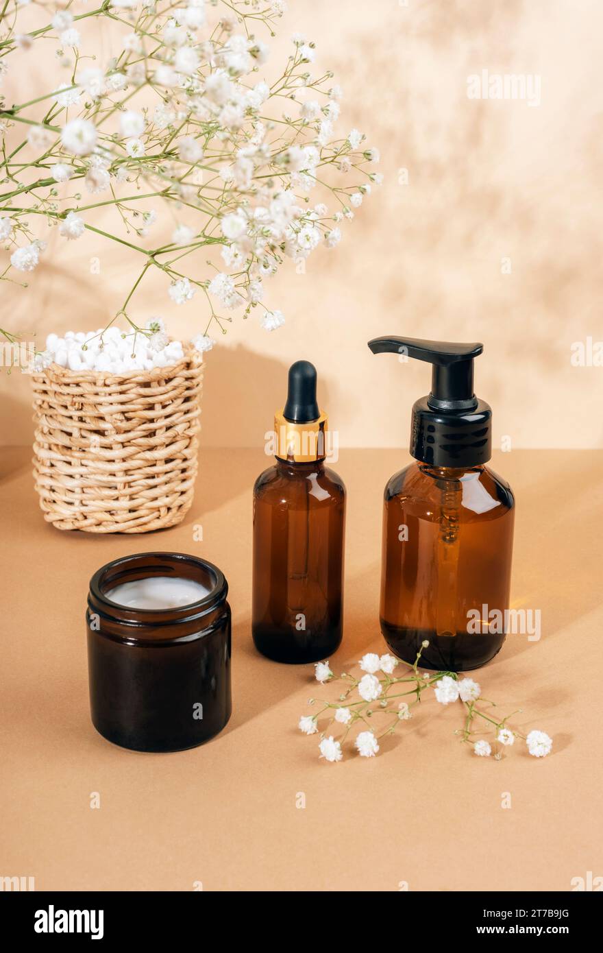 Detergente cosmetico per il viso, bottiglie di vetro marrone sierico, vaso crema e fiori bianchi gypsophila su sfondo beige chiaro. Cosmetici naturali, spa e benessere Foto Stock