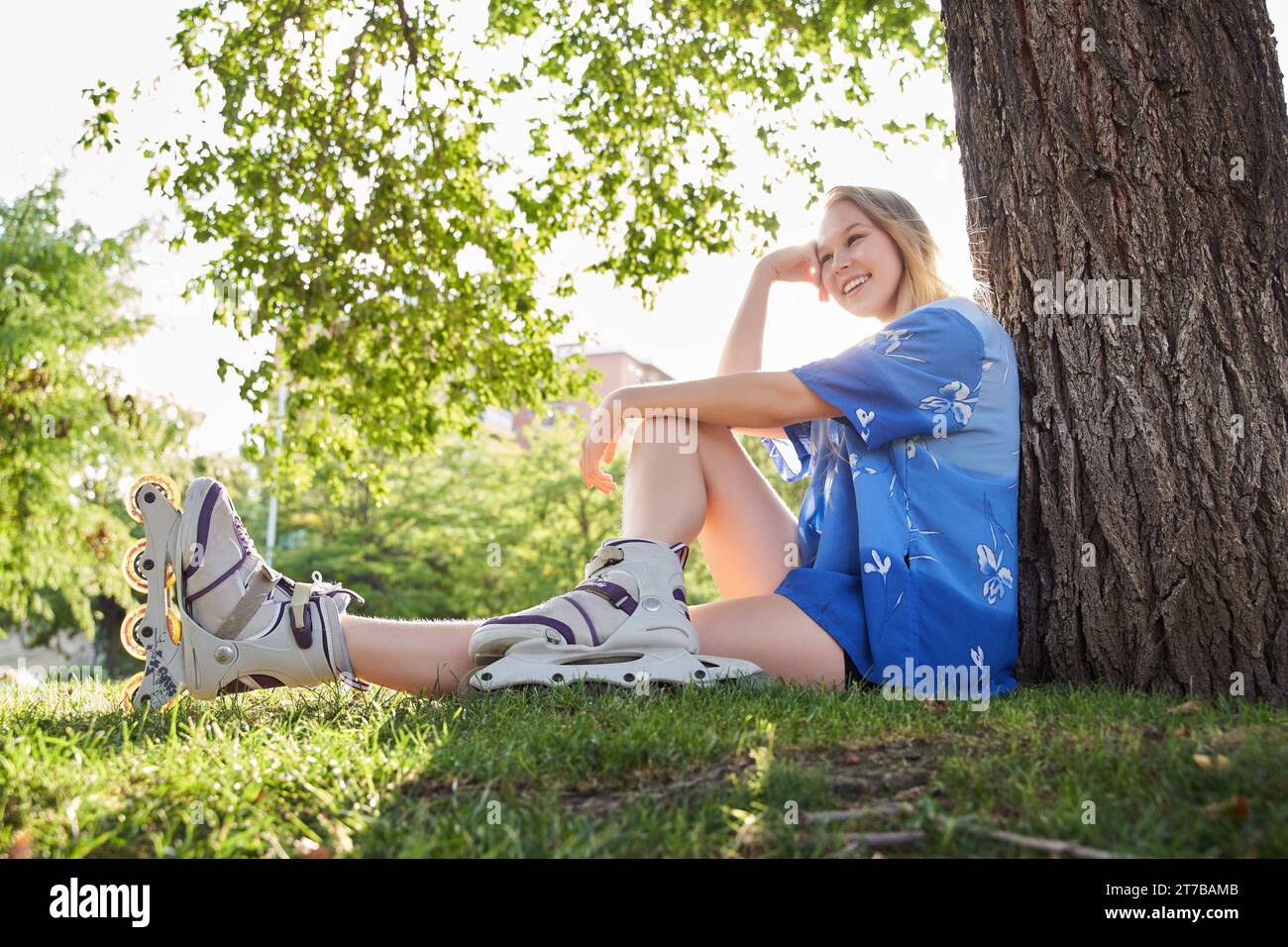 donna seduta in un parco su pattini in linea. il sole splende dietro di lei. Foto Stock