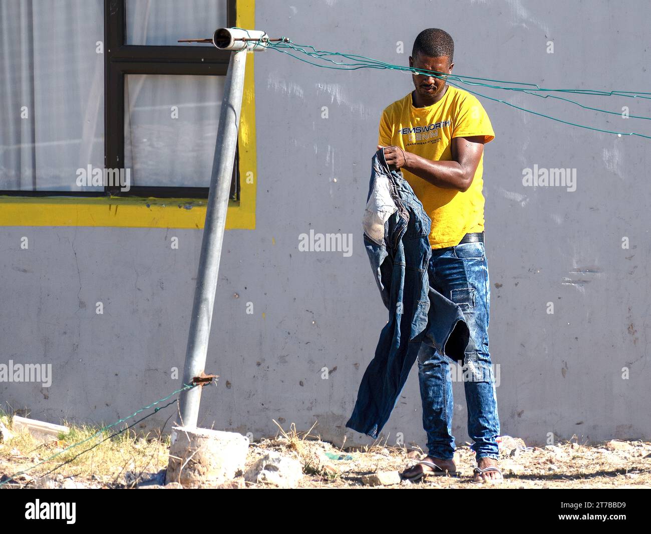 Un uomo africano che sbircia i suoi jeans davanti alla sua semplice casa in una cittadina in Sud Africa Foto Stock