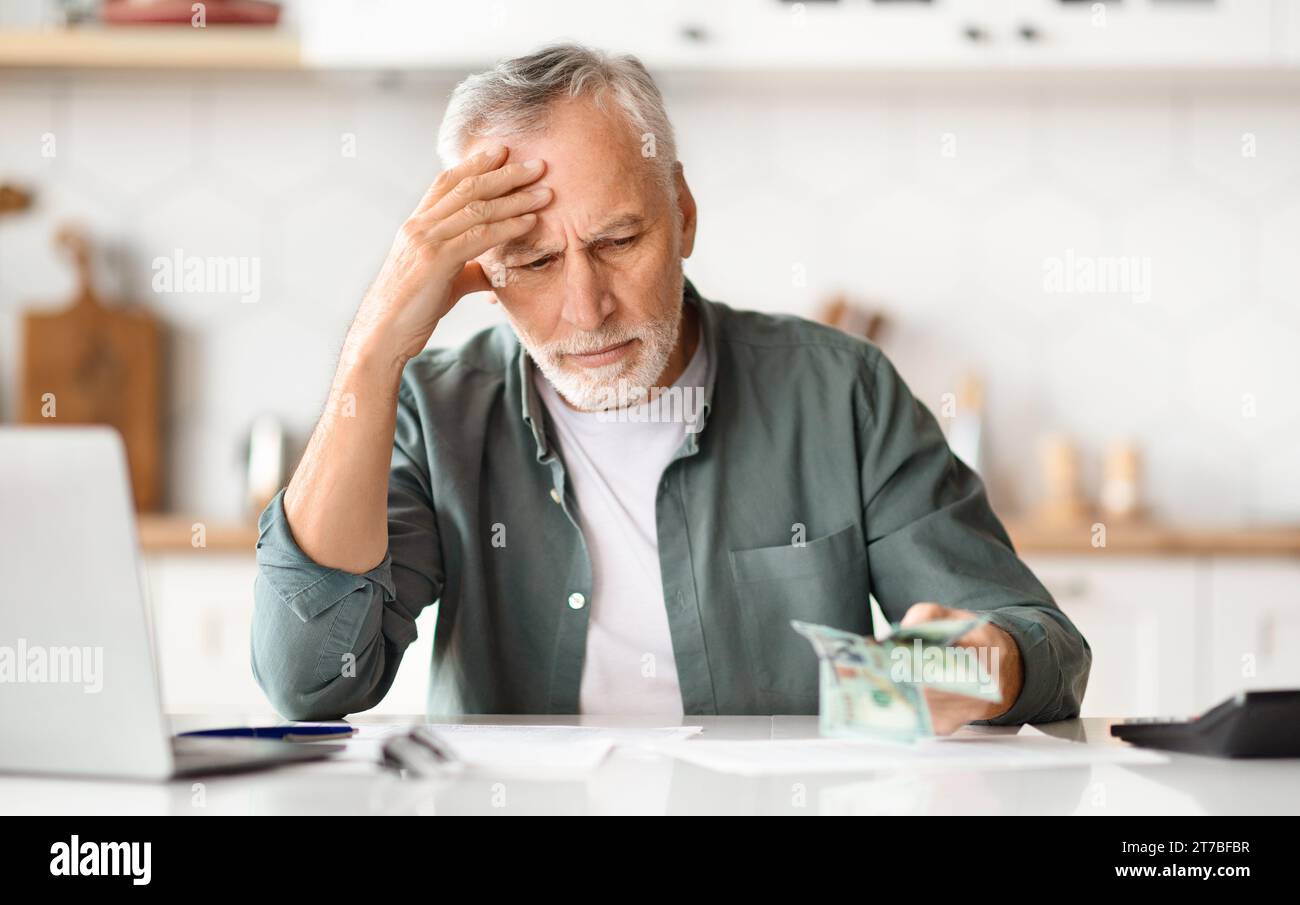 Problemi finanziari. Depresso Senior Man che guarda denaro contante in mano Foto Stock