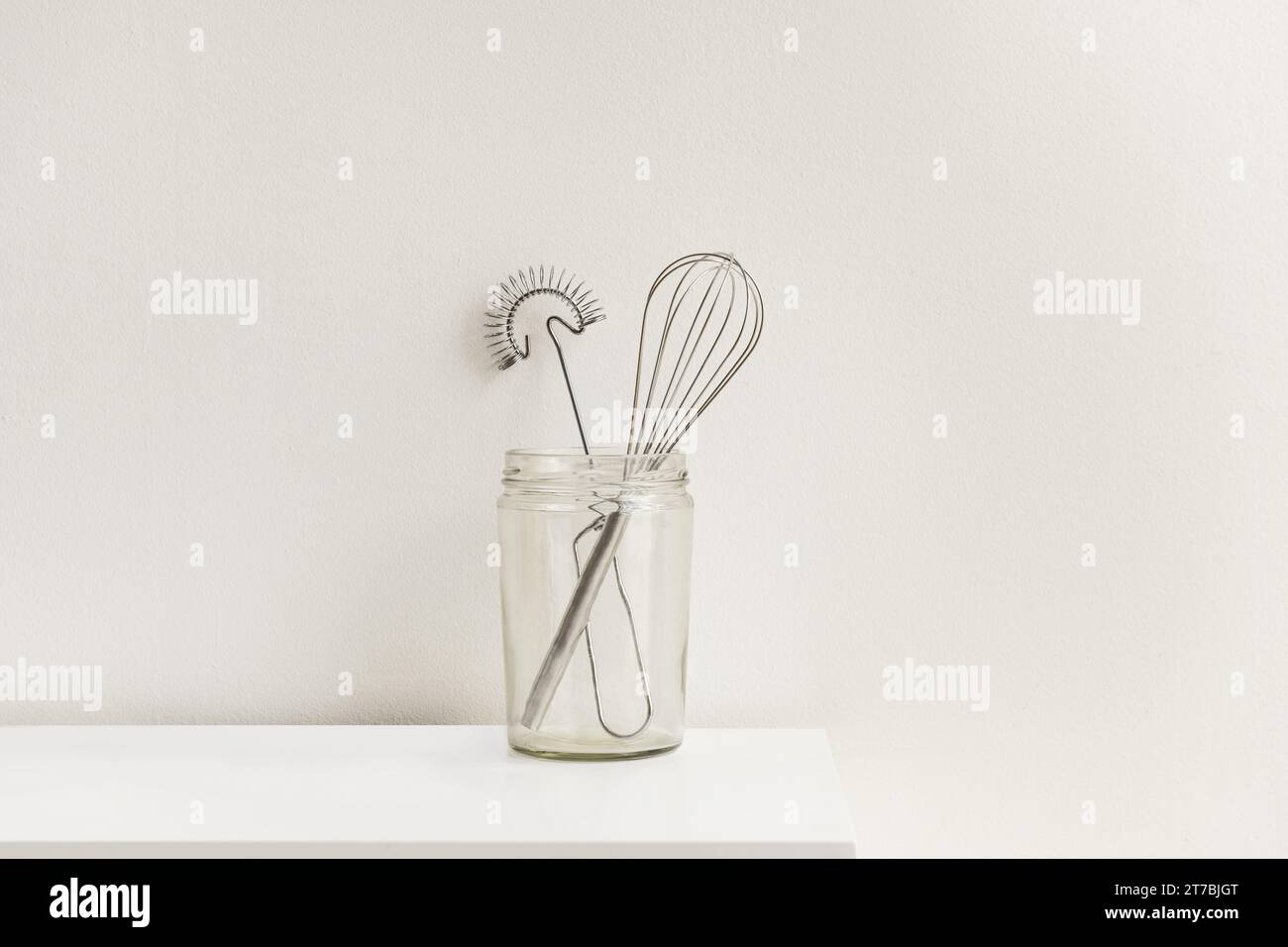 Un vaso in vetro trasparente con utensili da cucina in metallo Foto Stock