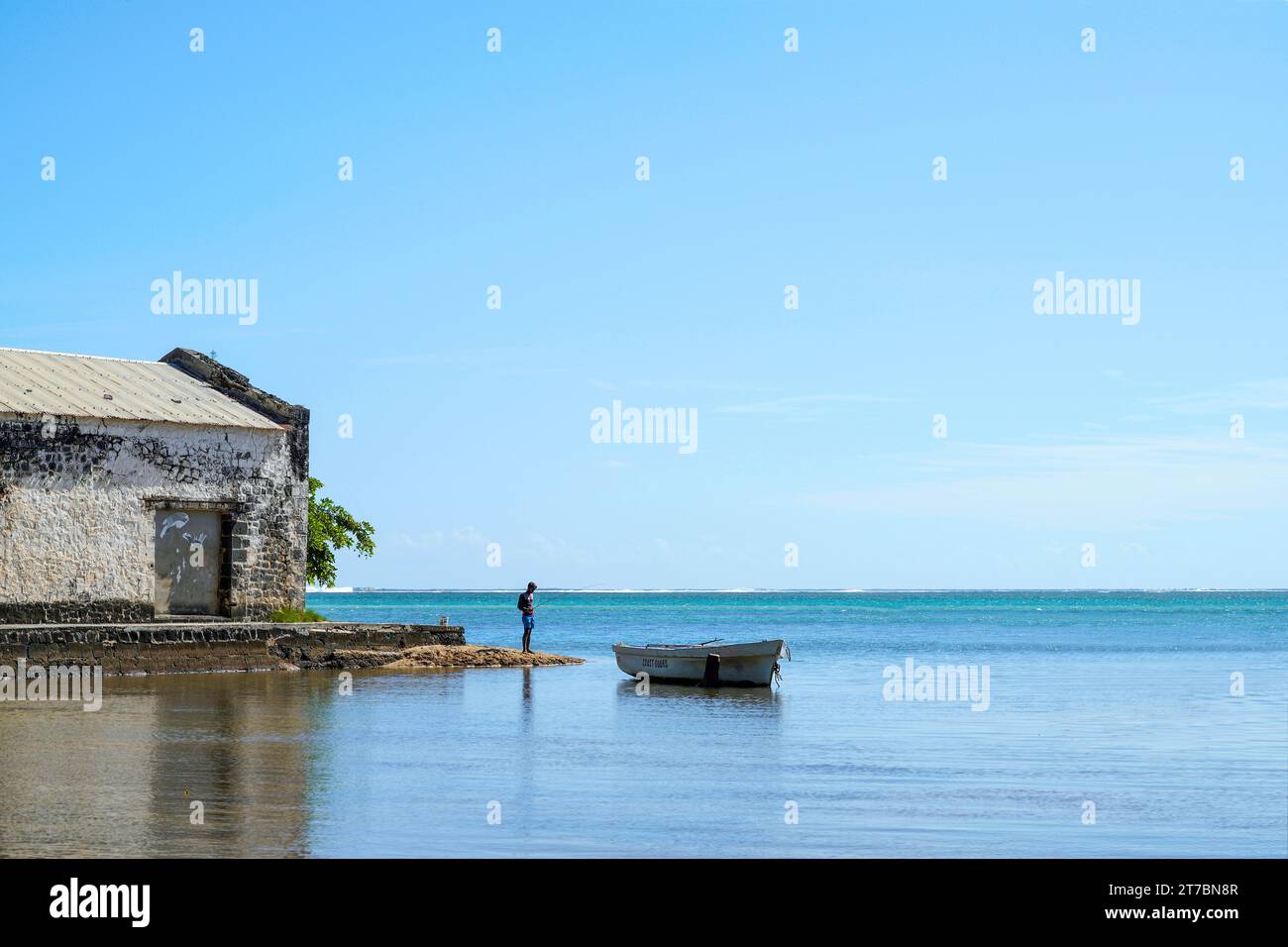 Un pescatore solitario che pesca sulle rive di una vecchia casa abbandonata fatta di pietra nel sud dell'isola di Mauritius. Foto Stock