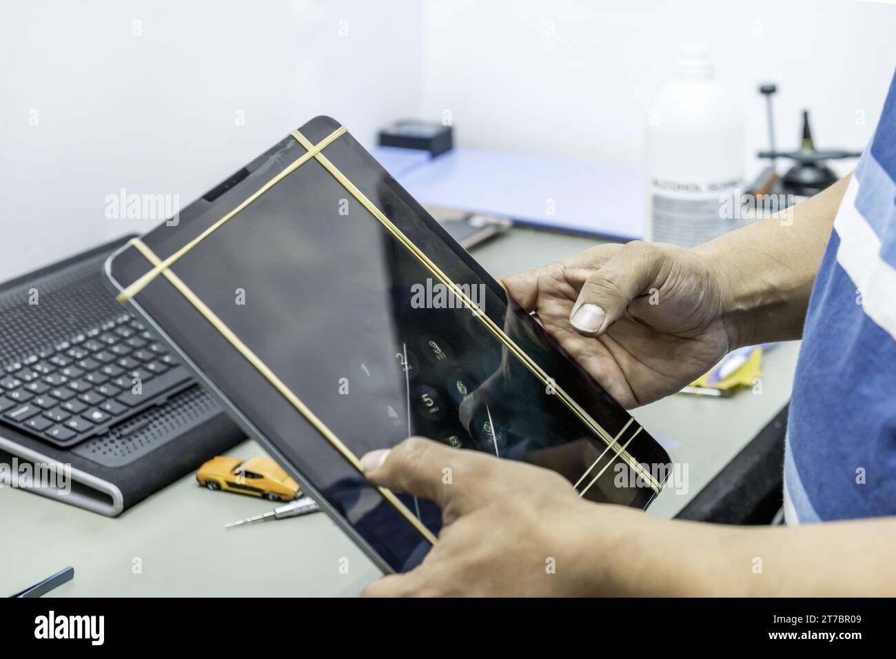 Un tecnico che ripara lo schermo di un tablet grande e sottile nella sua officina di elettronica Foto Stock