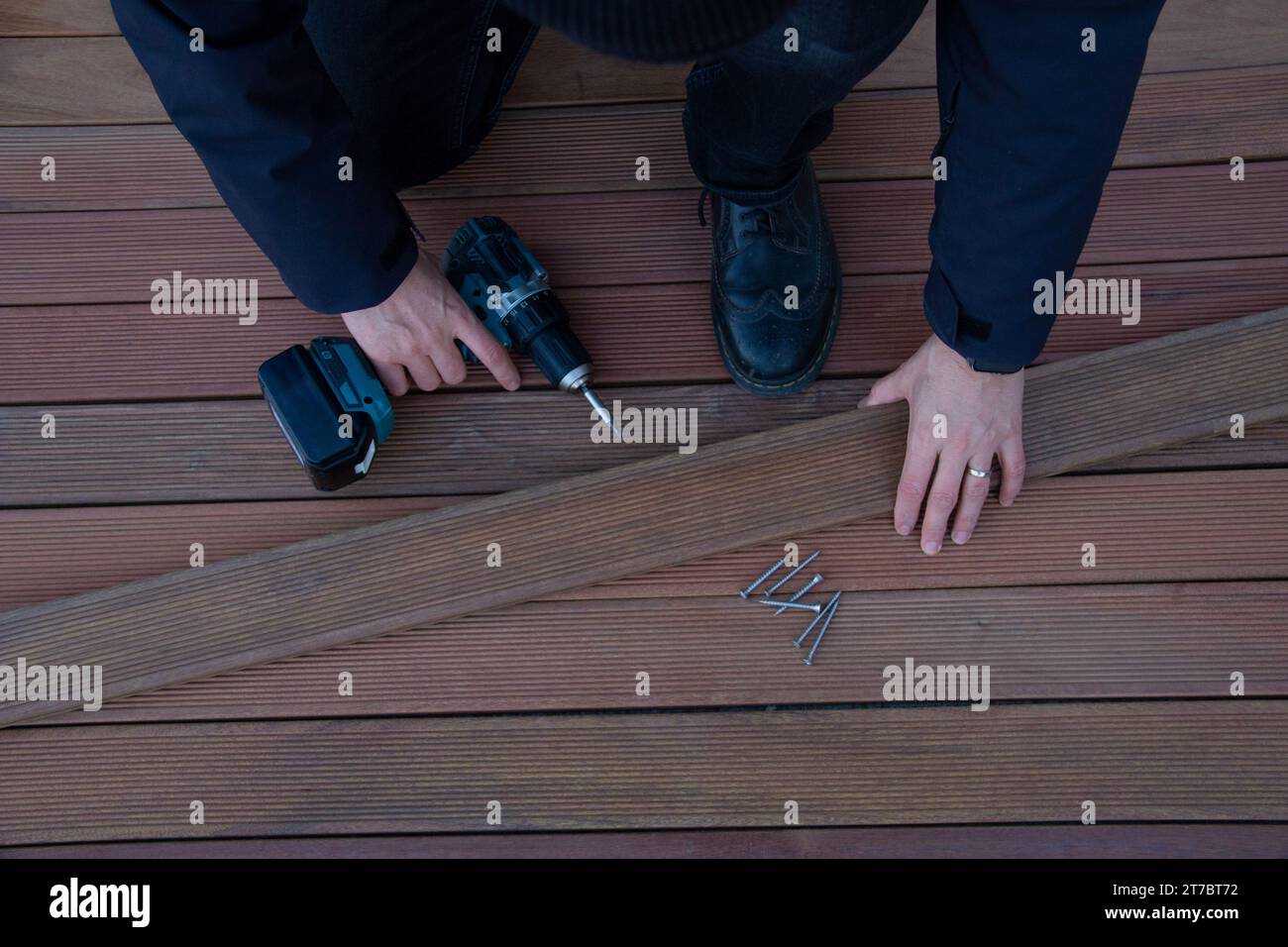 Lavoratore con terrazza che tiene il cacciavite elettrico e la tavola in legno, l'industria di pavimentazione in legno e l'edilizia Foto Stock