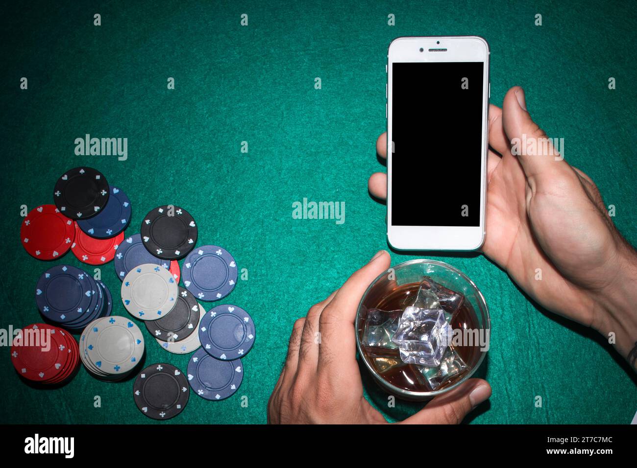 Mano del giocatore di poker che mostra il telefono cellulare che tiene il tavolo da poker in vetro del whiskey Foto Stock