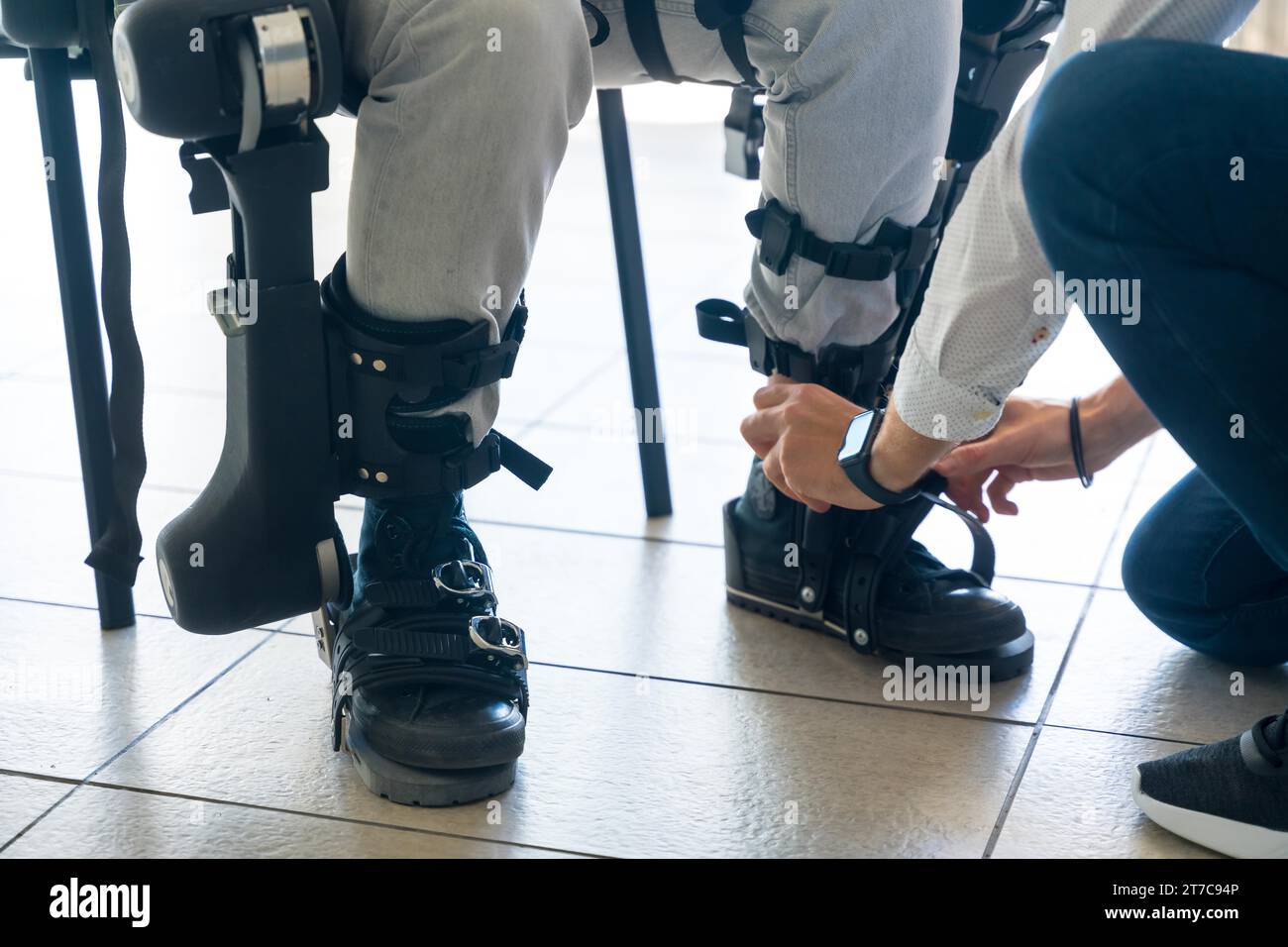 Esoscheletro meccanico, fisioterapista che posiziona i nastri sulle gambe della persona disabile per posizionare il suo scheletro robotico, fisioterapia in un moderno Foto Stock