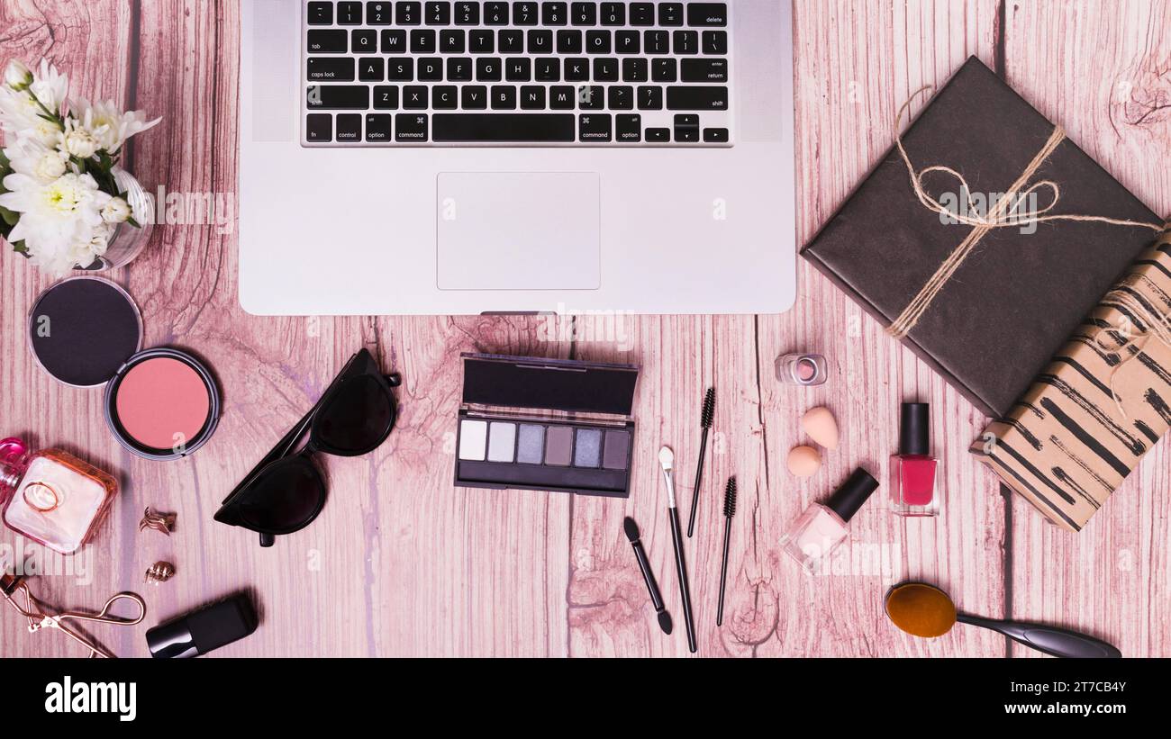 Computer portatile con diario di prodotti cosmetici sfondo in legno rosa Foto Stock