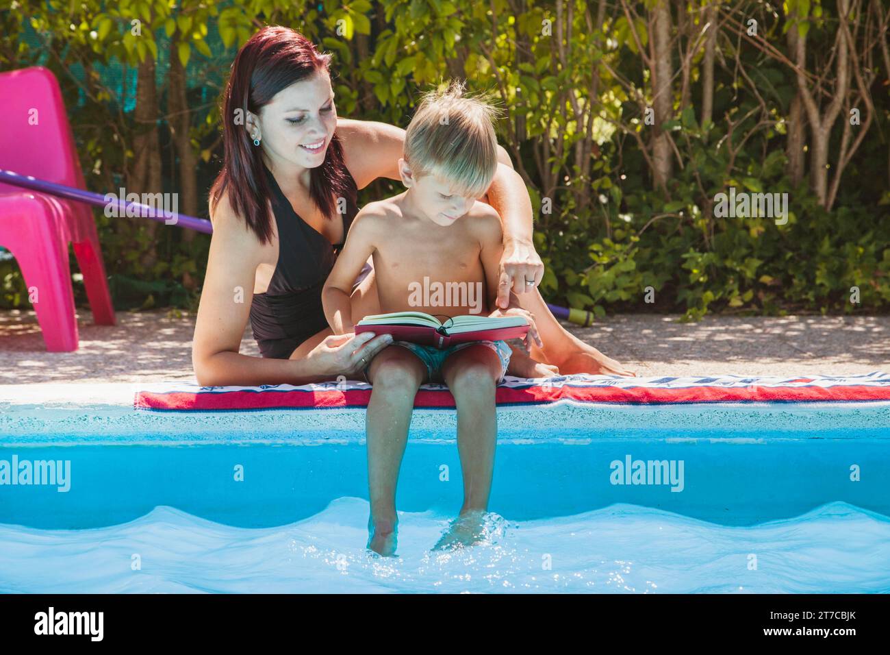 Madre e figlio seduto vicino alla piscina a leggere Foto Stock