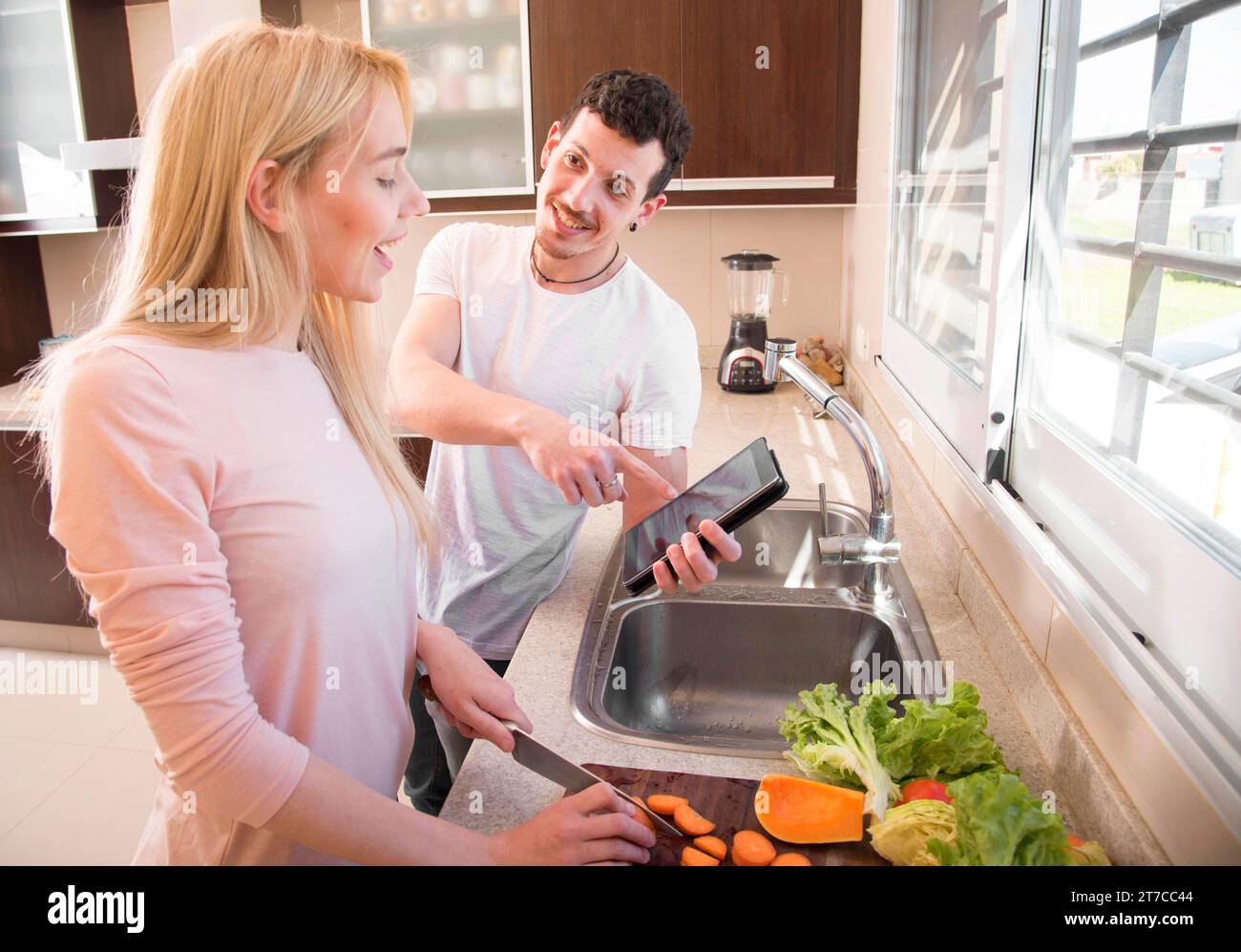 Uomo sorridente che mostra un tablet digitale sua moglie che taglia carote Foto Stock
