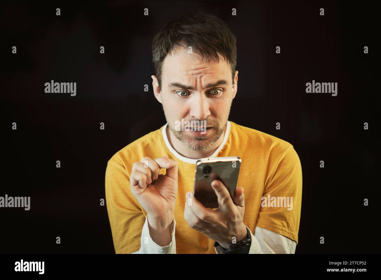 Cattive notizie sullo smartphone. Un uomo guarda un messaggio sul suo cellulare con gli occhi spalancati e la bocca aperta. È scioccato e spaventato. Emozioni umane su bla Foto Stock