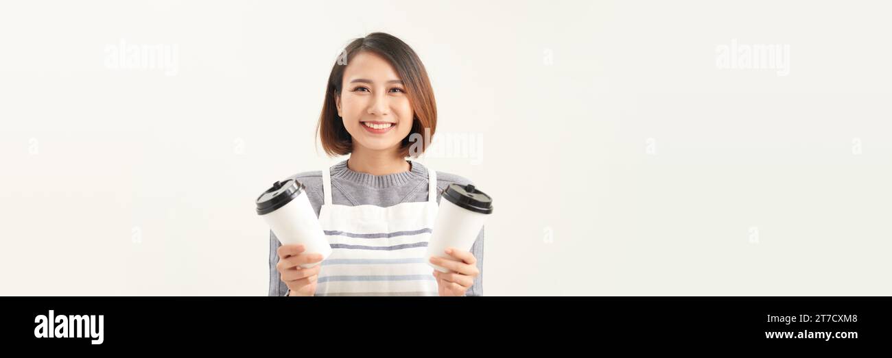 Simpatica e sorridente giovane donna asiatica in grembiule che regala caffè, tè e bevande calde Foto Stock