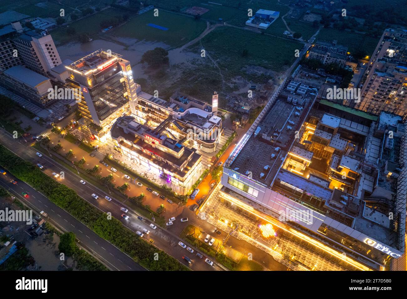 Ripresa aerea con drone che mostra edifici a più piani illuminati con centri commerciali, uffici, strade trafficate e case Foto Stock