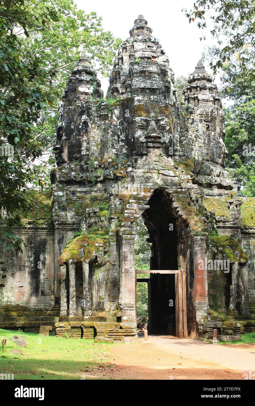 Gigantesche teste di pietra scolpite si trovano in cima a un cancello di Angkor Thom presso il Parco Archeologico di Angkor, Cambogia. Muschio, lichene e ocra rossa colorano le pareti Foto Stock