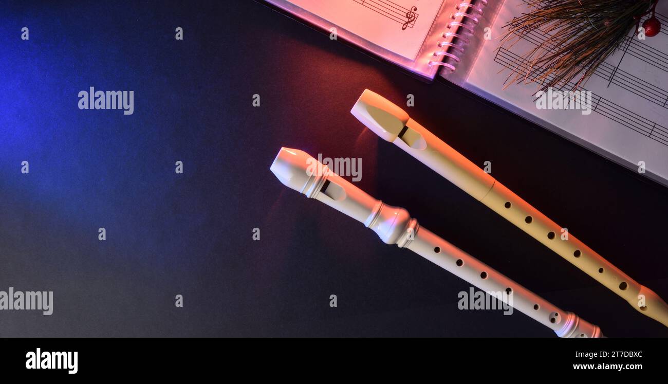 Sfondo per eventi musicali a fiato con dettagli di due registratori in plastica tradizionali su un tavolo nero con cartella spartiti. Vista dall'alto. Foto Stock