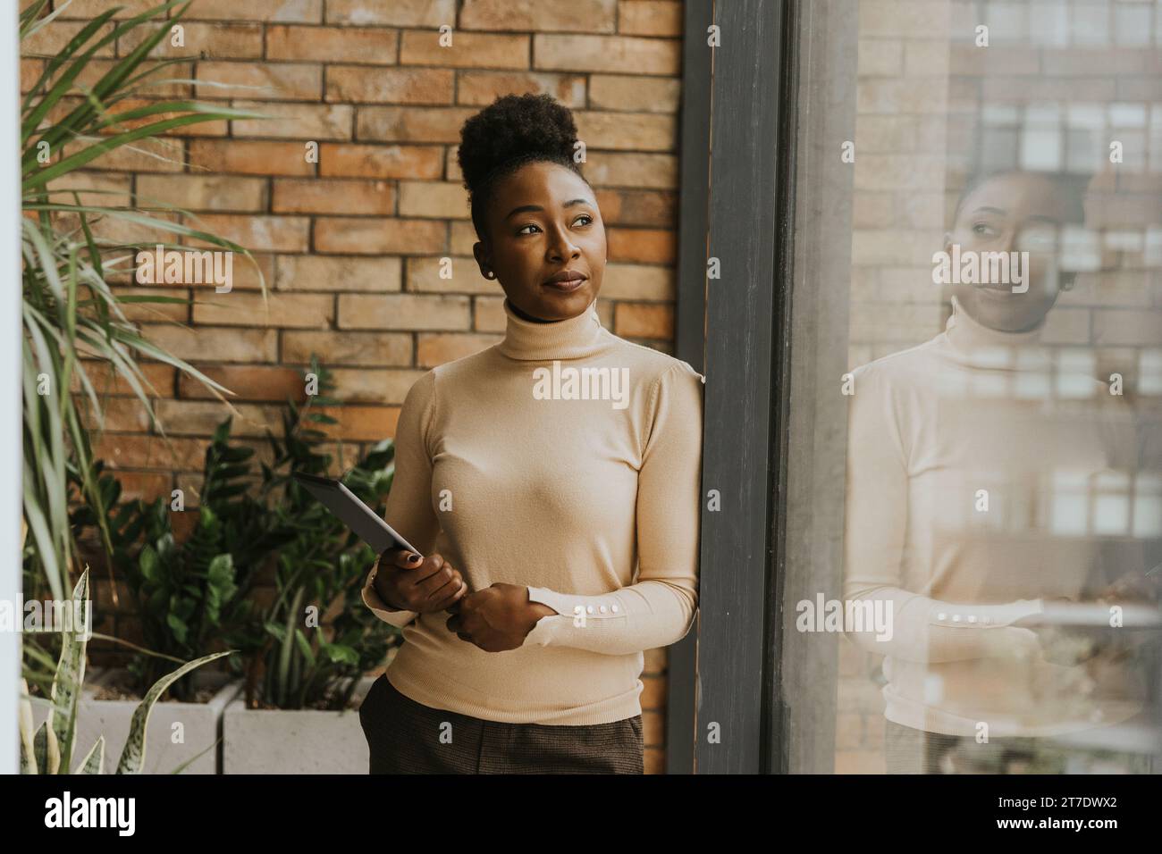 Una bella giovane donna d'affari afroamericana con un tablet digitale in piedi accanto al muro in stile industriale Foto Stock