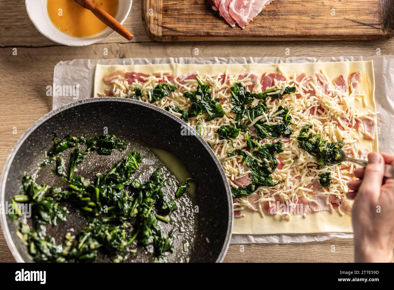 Il cuoco prepara mini torte per pizza, mette gli spinaci su sfoglia con formaggio e pancetta - vista dall'alto. Procedura di ricetta: 4 di 10 Foto Stock