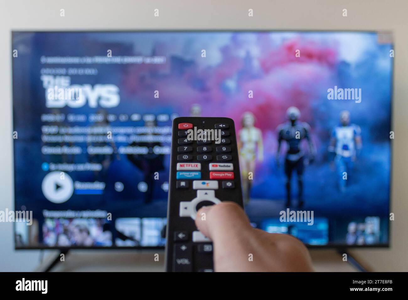 Primo piano con la mano destra maschio che regge un telecomando smart tv nero con interfaccia di streaming Amazon prime sullo sfondo Foto Stock