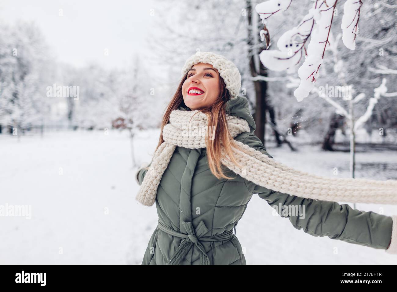 Giovane donna felice che gira nel parco invernale innevato indossando abiti caldi a maglia e divertendosi all'aperto. Ragazza che si gode il tempo invernale. Attività stagionali Foto Stock