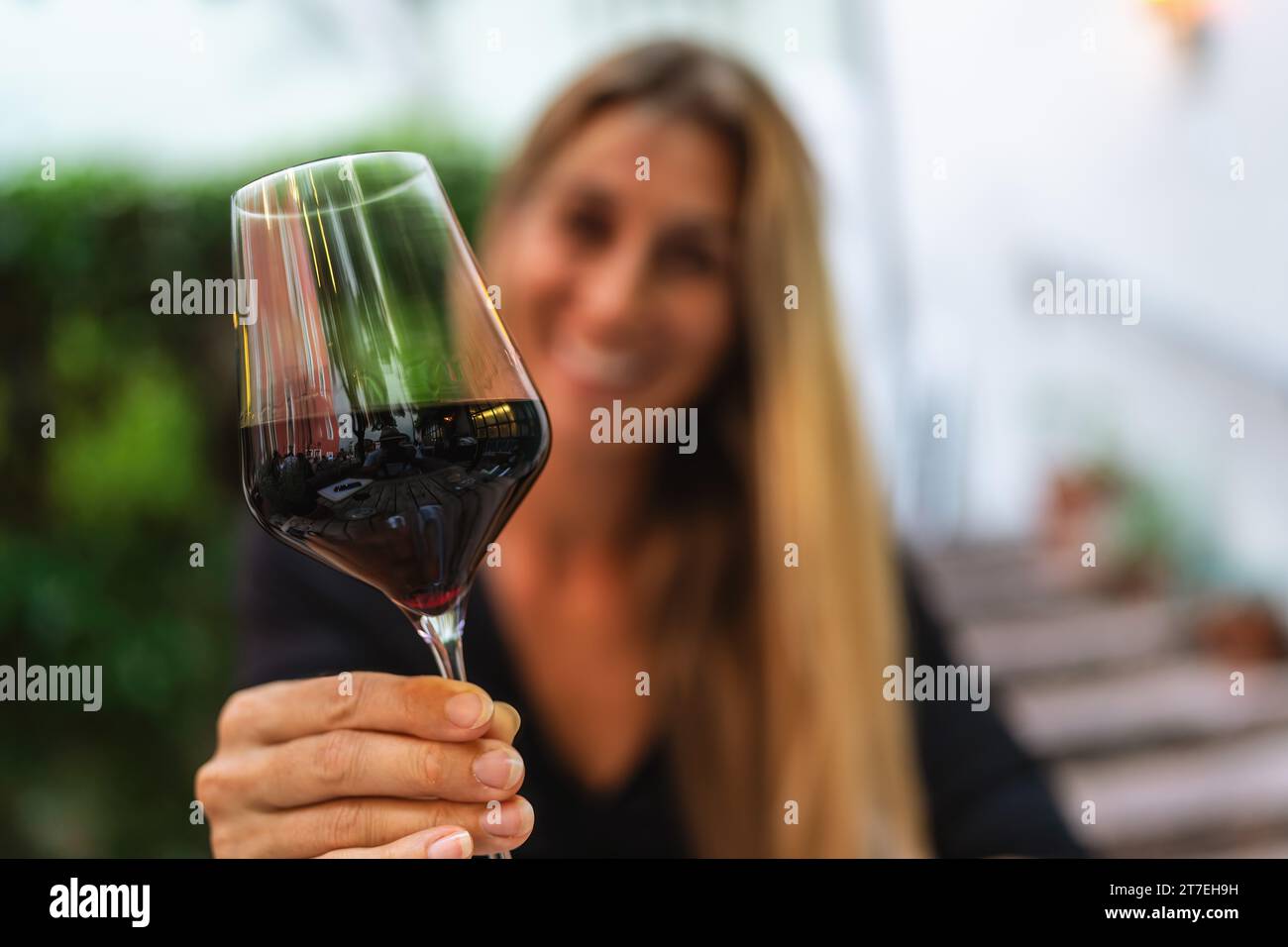 Donna che tosta con un bicchiere di vino rosso, sfondo sfocato Foto Stock