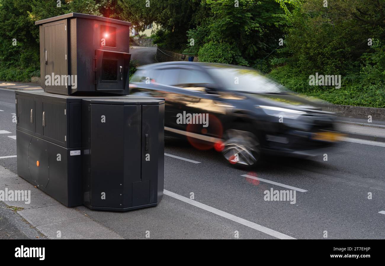 Telecamera per l'applicazione della velocità sul lato della strada con un'auto con sfocatura del movimento ad alta velocità e sfondo fogliame Foto Stock