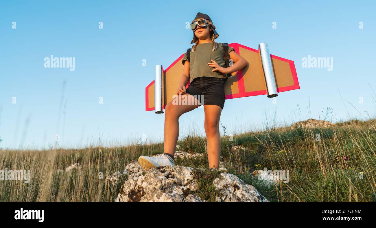 Bambino in costume da pilota con ali di cartone in piedi su una roccia all'aperto Foto Stock