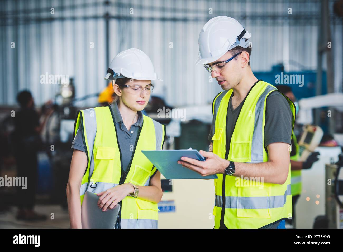 Team di ingegneri meccanici che tiene un elenco di controllo su appunti e penne in un'officina siderurgica. Software di programmazione per robot industriali per la produzione automatizzata Foto Stock