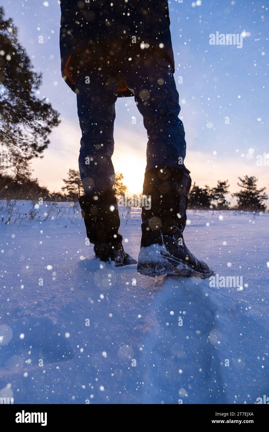 Un viaggiatore con gli scarponi cammina lungo una strada invernale innevata. Foto Stock