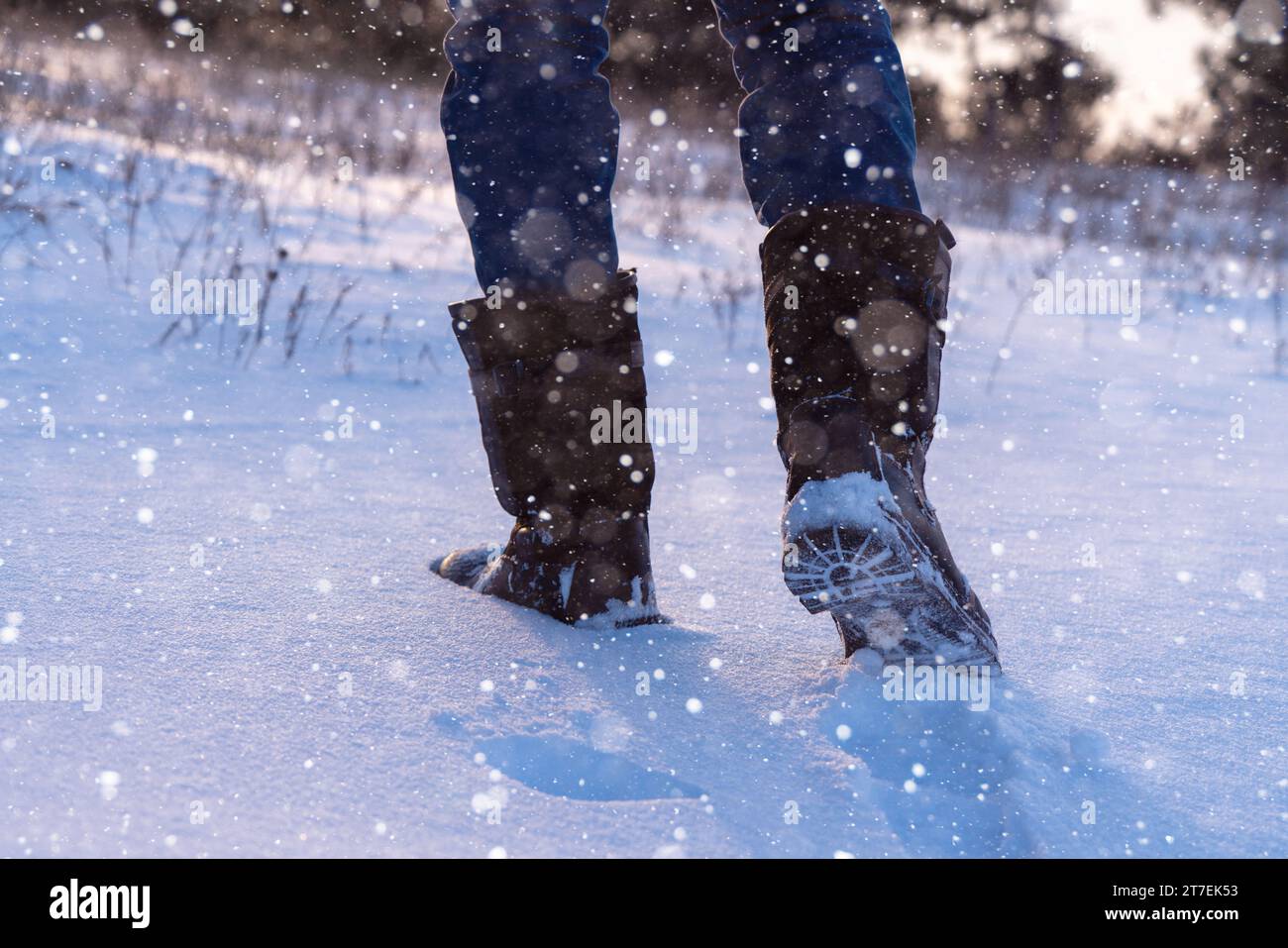 Un viaggiatore con gli scarponi cammina lungo una strada invernale innevata. Foto Stock
