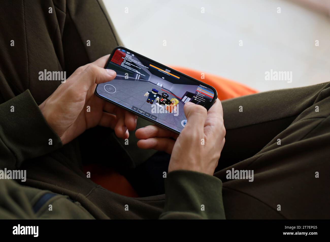 Roblox per dispositivi mobili iOS: Schermo dello smartphone su iPhone 15 in mani maschili durante il gioco mobile. Giochi e intrattenimento mobili su dispositivi portatili Foto Stock