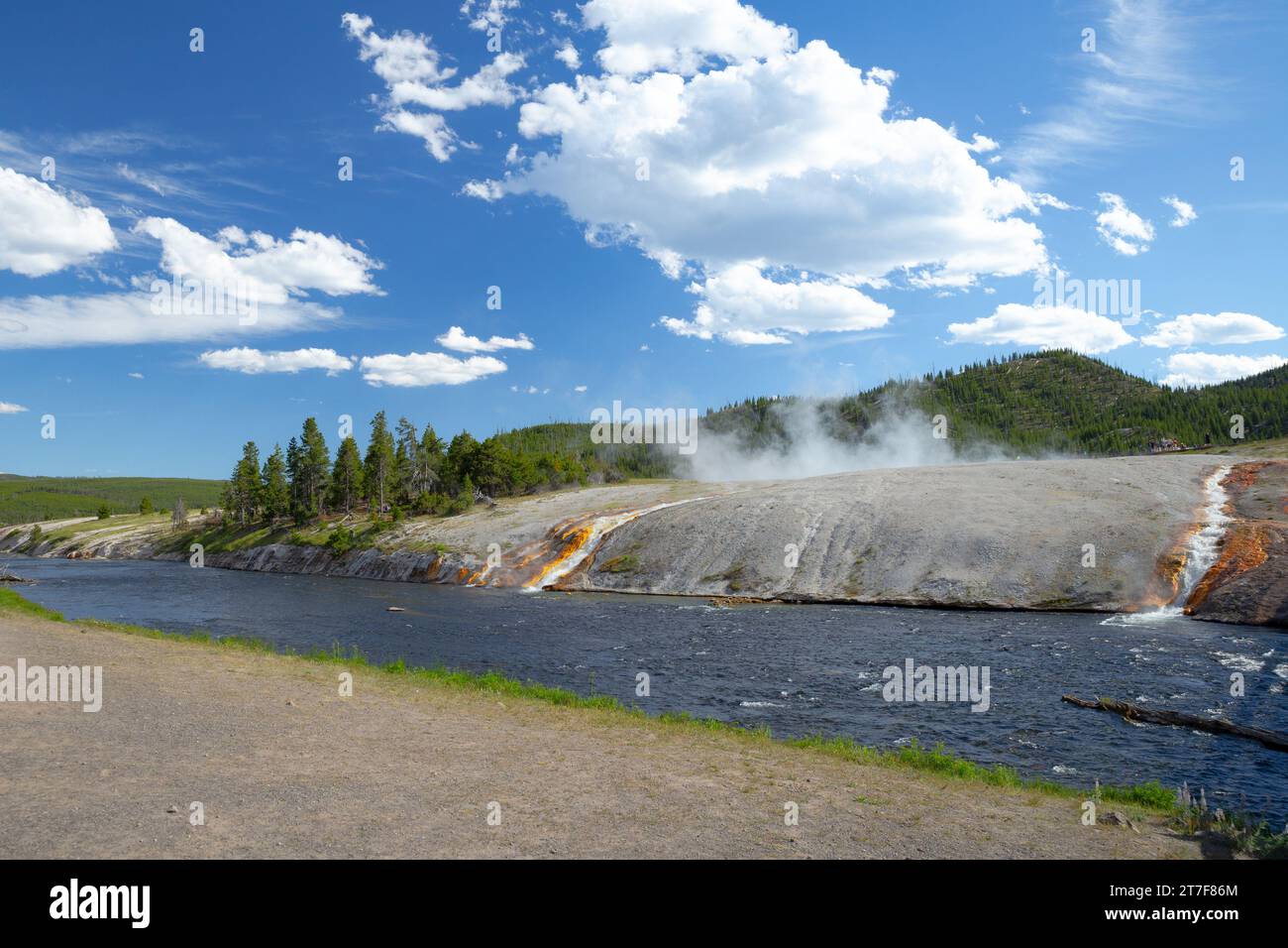 l'acqua termale calda scorre attraverso una roccia con vapore che sale e foresta Foto Stock