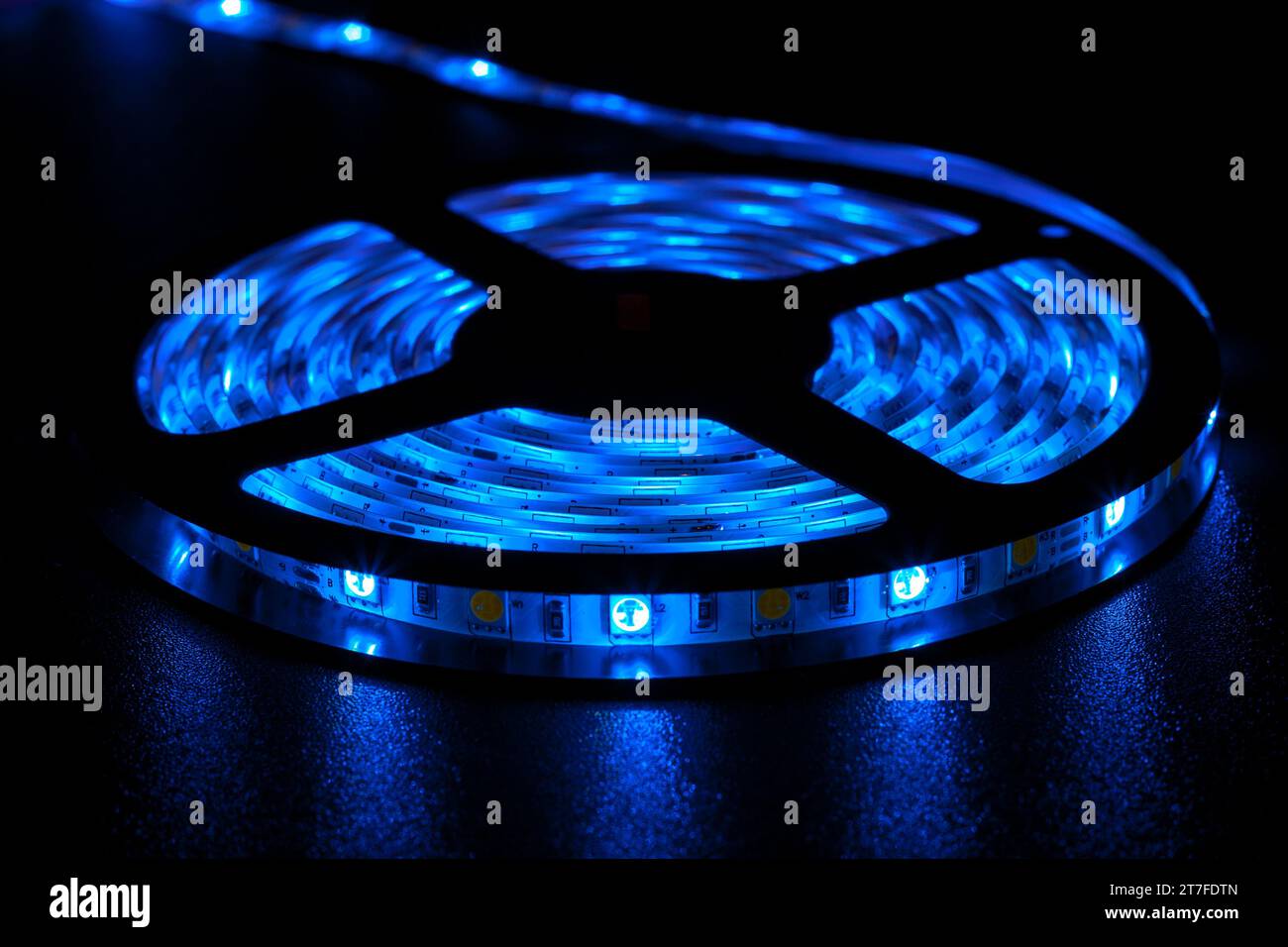 Rotolo di striscia LED inseguibile con lampade blu neon luminose posizionate sul tavolo in ambienti bui Foto Stock