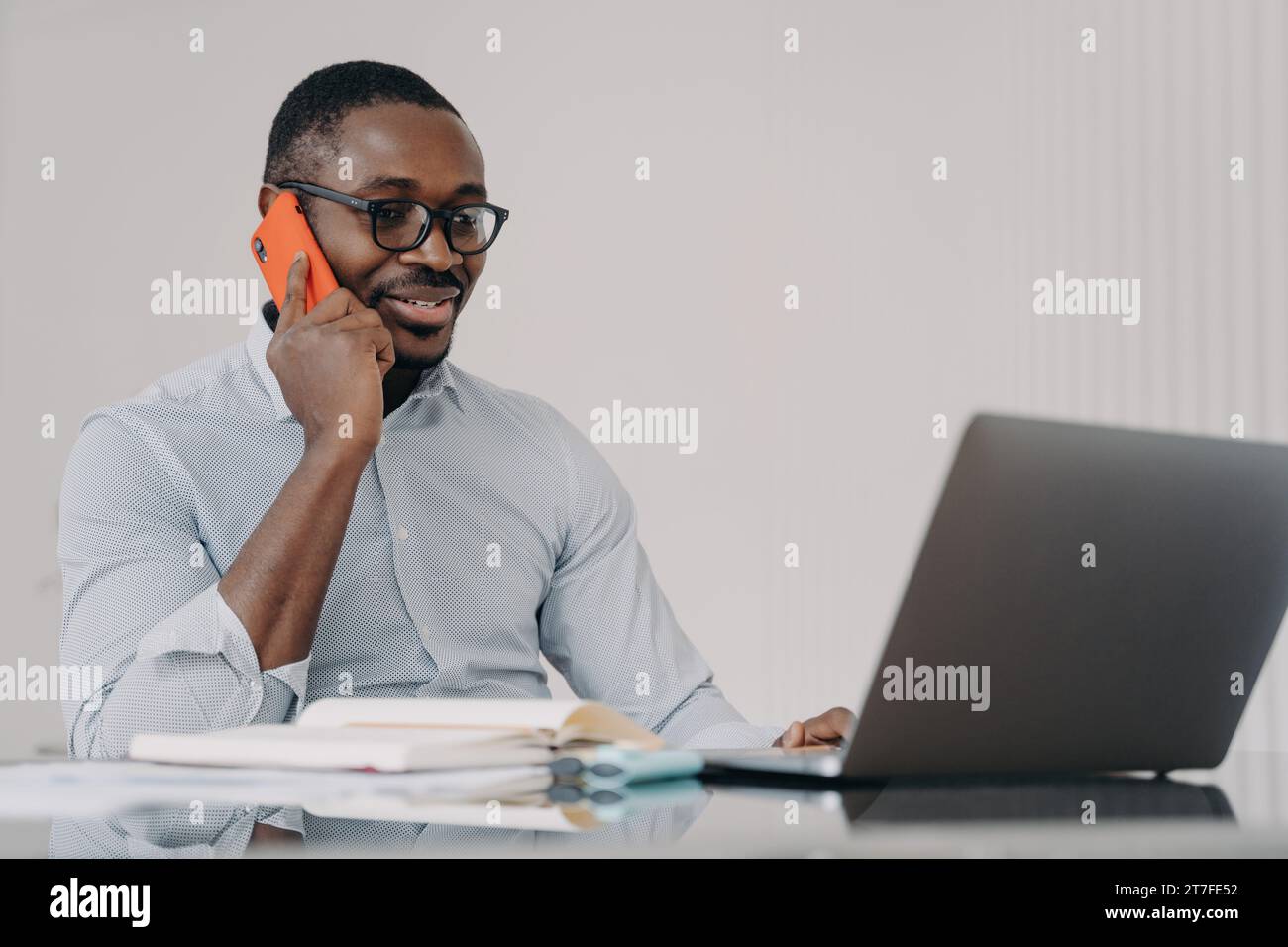 Uomo d'affari con gli occhiali al telefono, che lavora al computer portatile in un ufficio moderno Foto Stock
