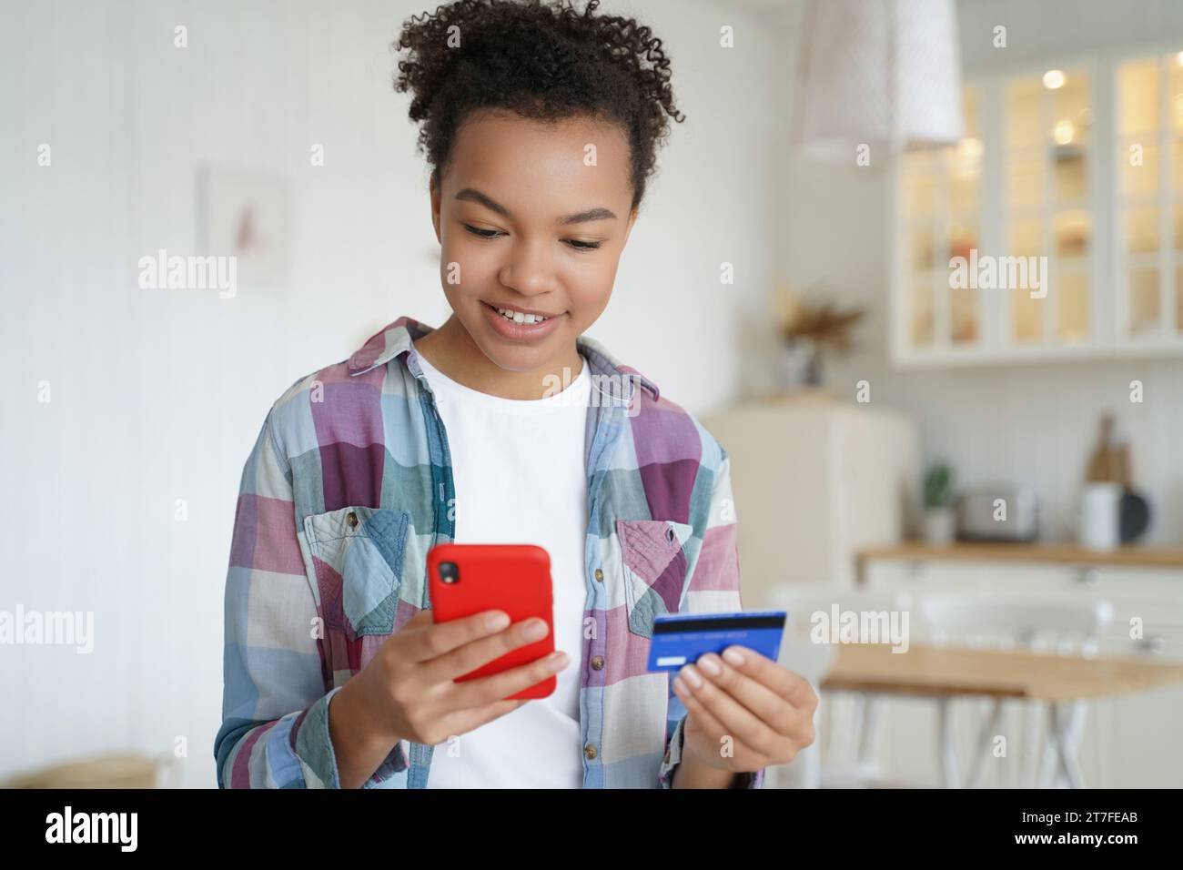 Un adolescente nero che fa shopping online con un telefono e una carta di credito, sorridendo Foto Stock