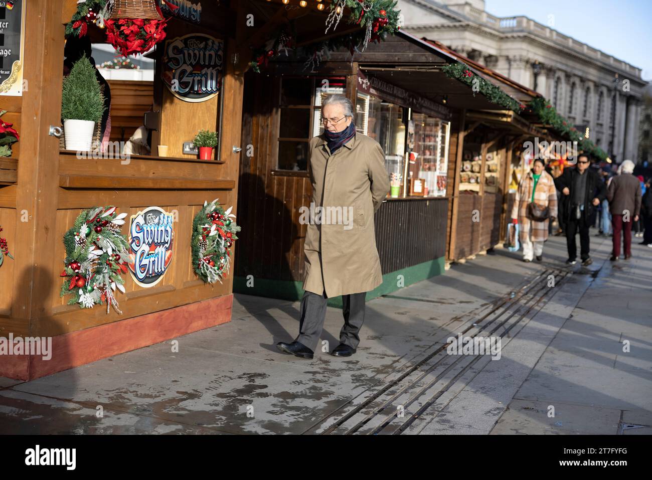 Un uomo cammina attraverso i mercatini di Natale di Trafalgar Square e le capanne festive , Londra, Inghilterra, Regno Unito. Novembre 2023 Foto Stock