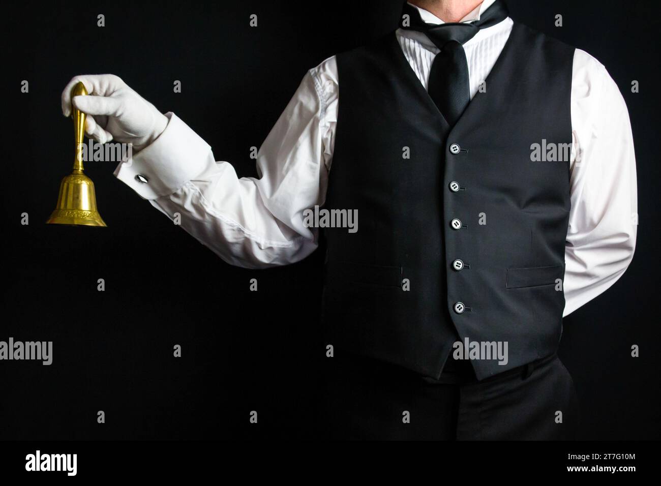 Ritratto del maggiordomo o del concierge dell'hotel con gilet e guanti bianchi con campana d'oro. Concetto di anello per manutenzione. Foto Stock