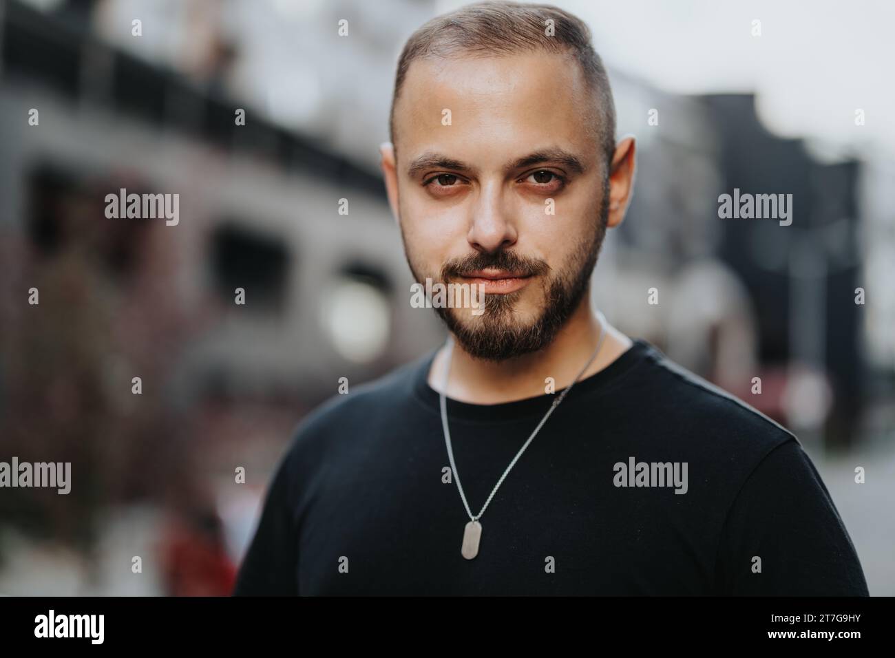 Un giovane sicuro e attraente che si posa all'aperto. Sorride e guarda la telecamera, in piedi con stile e con un comportamento di successo. Foto Stock