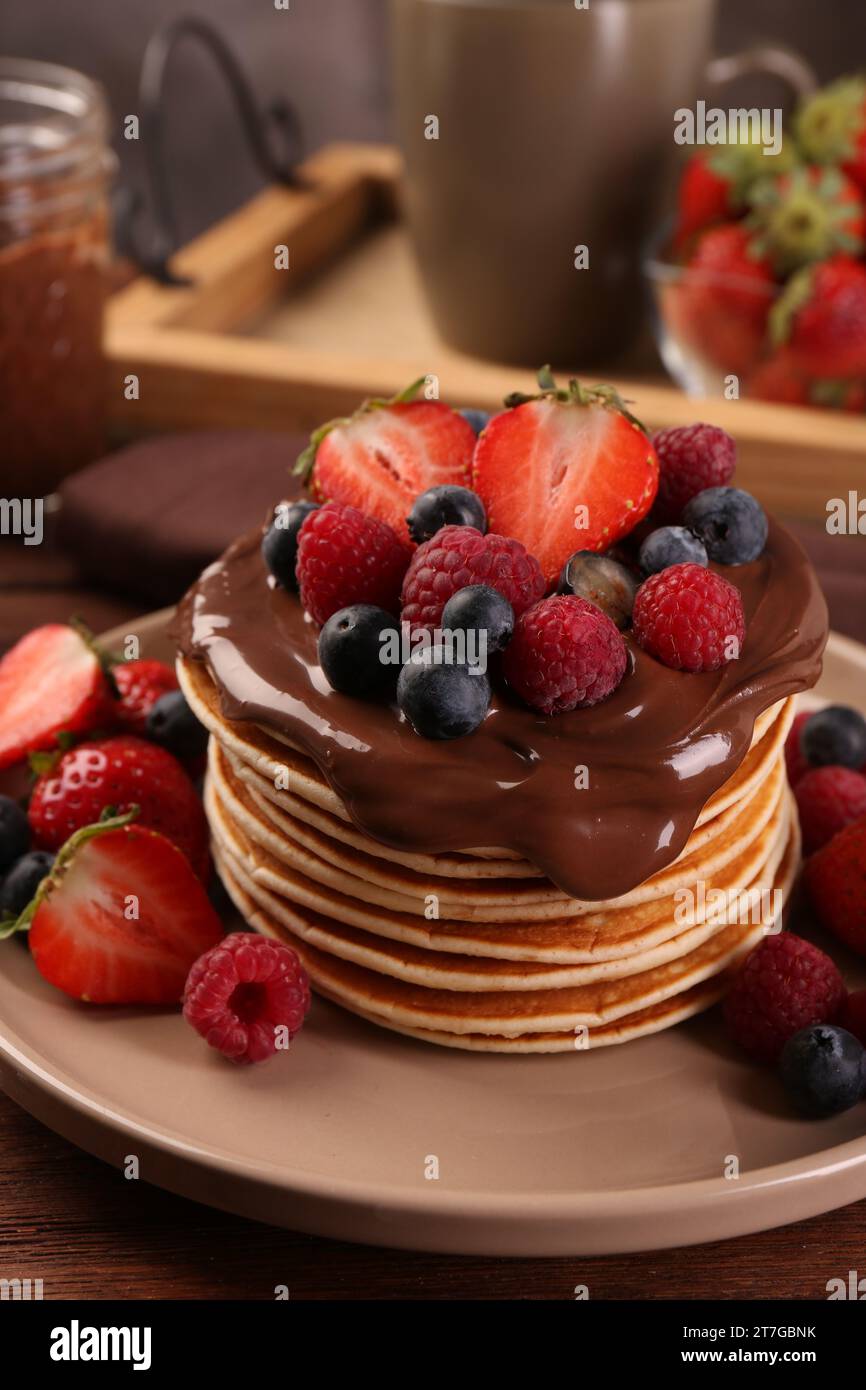 Pila di gustosi pancake con frutti di bosco freschi e cioccolato spalmato sul tavolo, primo piano Foto Stock