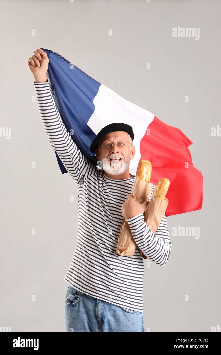 Uomo anziano con baguette e bandiera della Francia su sfondo chiaro Foto Stock