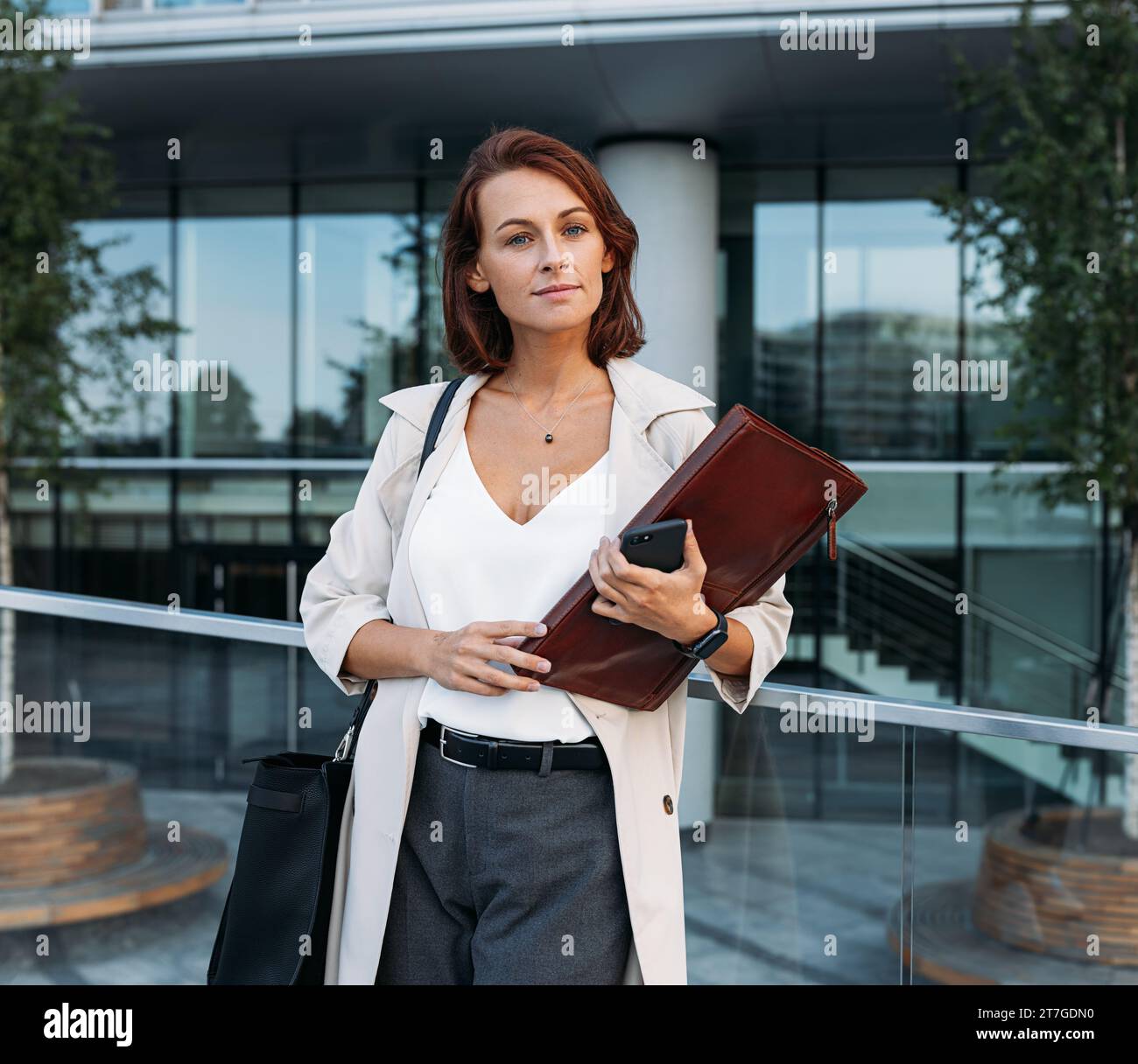 Donna elegante con cartella in pelle all'aperto. Donna d'affari con capelli di zenzero in piedi all'aperto. Foto Stock