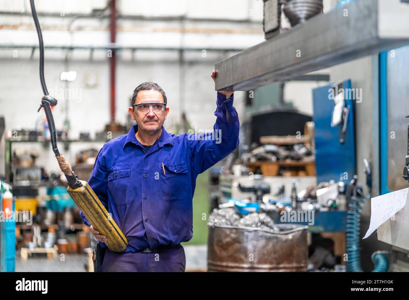 Operatore operante in fabbrica nel settore del controllo numerico che fornisce una parte in metallo rialzato su una macchina a un cliente, una fabbrica industriale Foto Stock