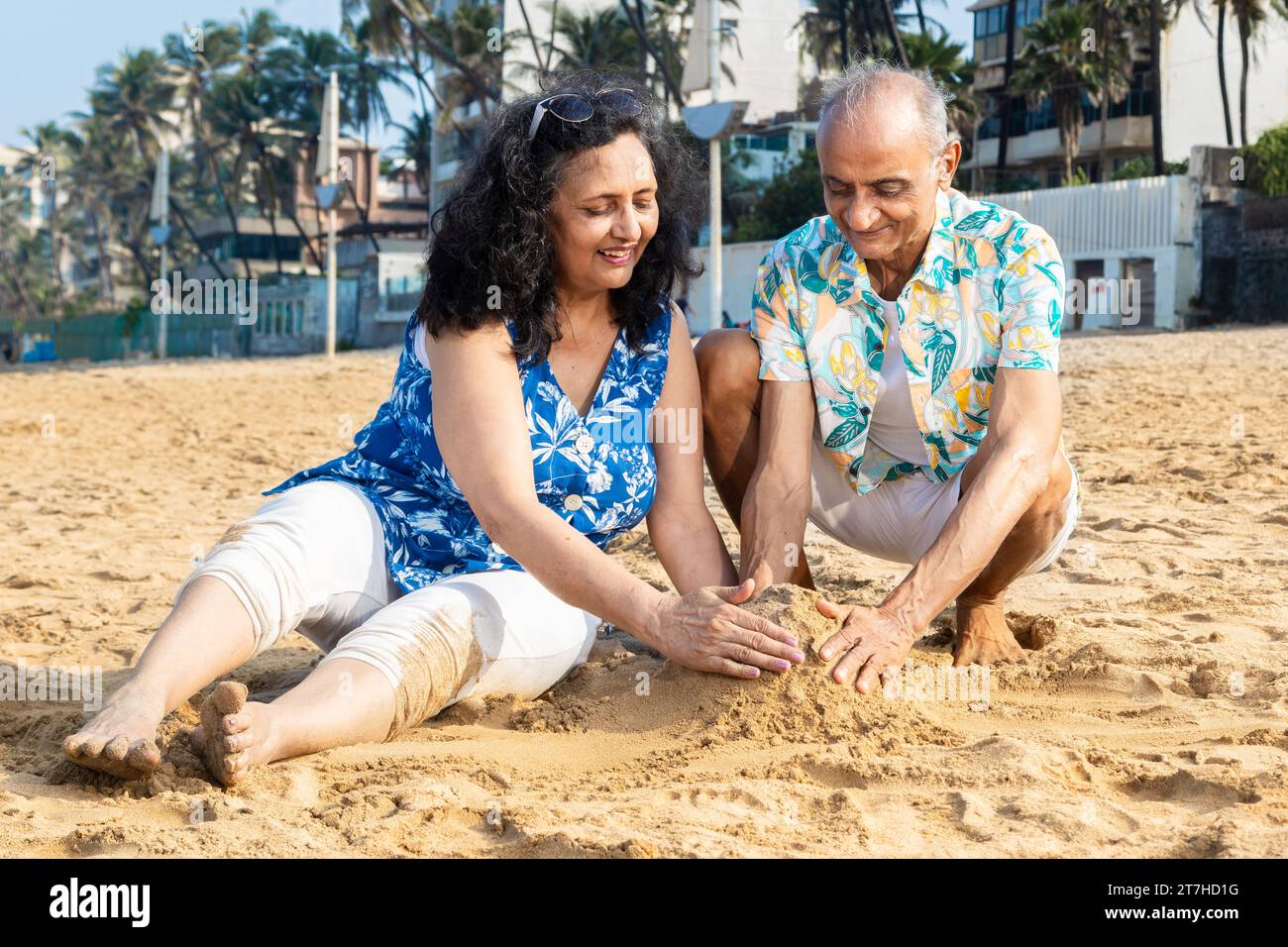 Felice coppia indiana anziana che fa castello di sabbia o casa sulla spiaggia per godersi la vacanza. Foto Stock