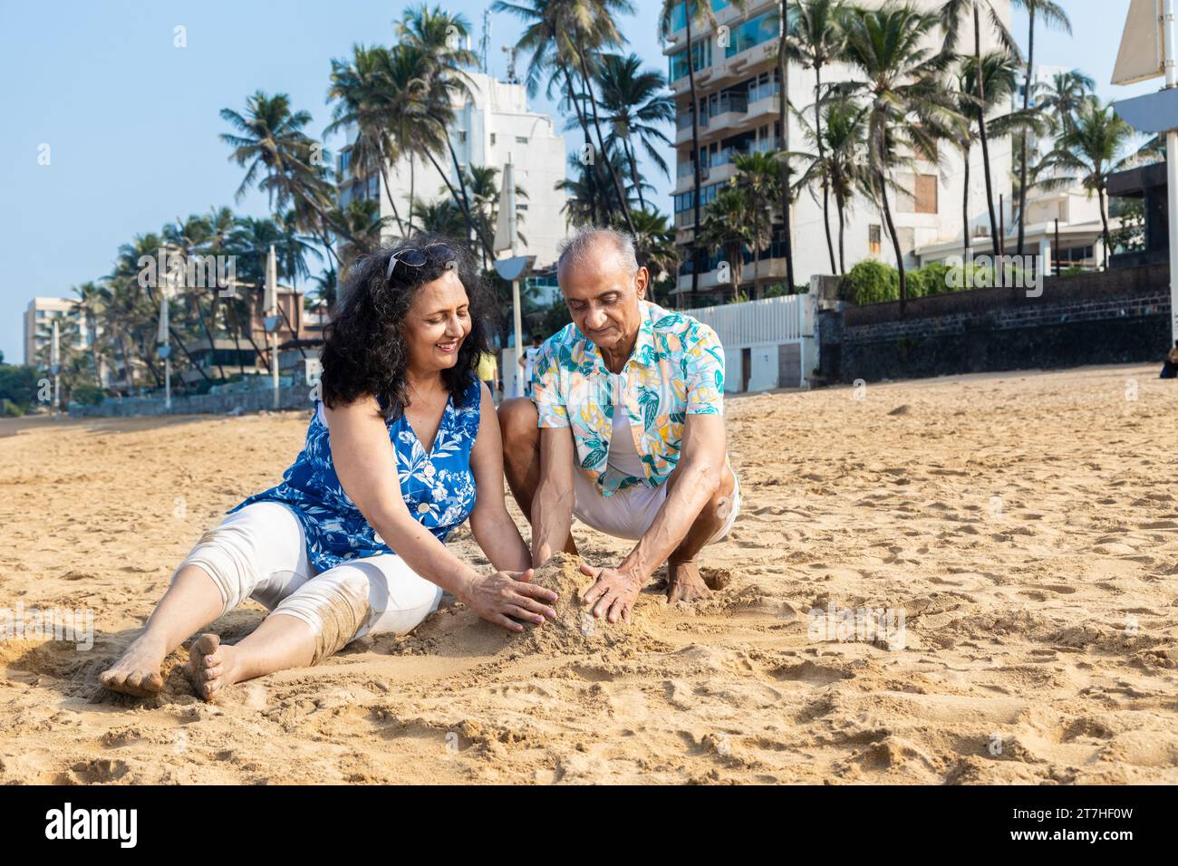 Felice coppia indiana anziana che fa castello di sabbia o casa sulla spiaggia per godersi la vacanza. Foto Stock
